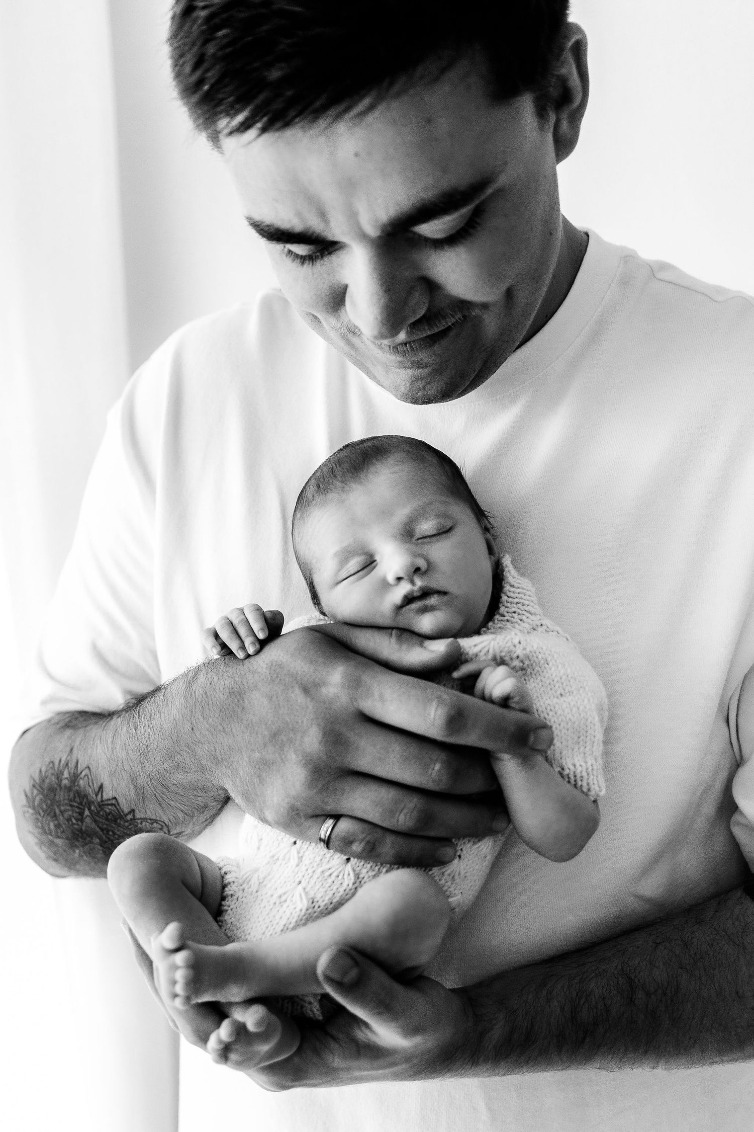Father tenderly holds sleeping newborn baby in his arms, black and white portrait.