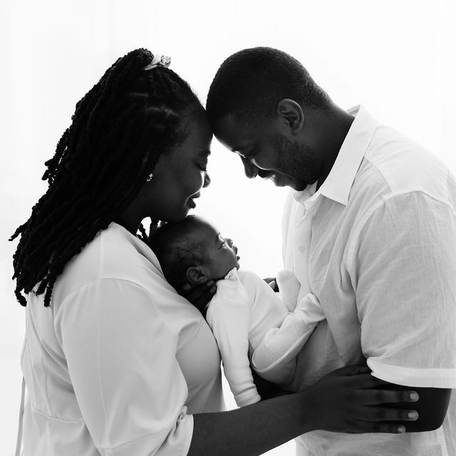 Black and white portrait of loving parents cradling their sleeping newborn baby together.