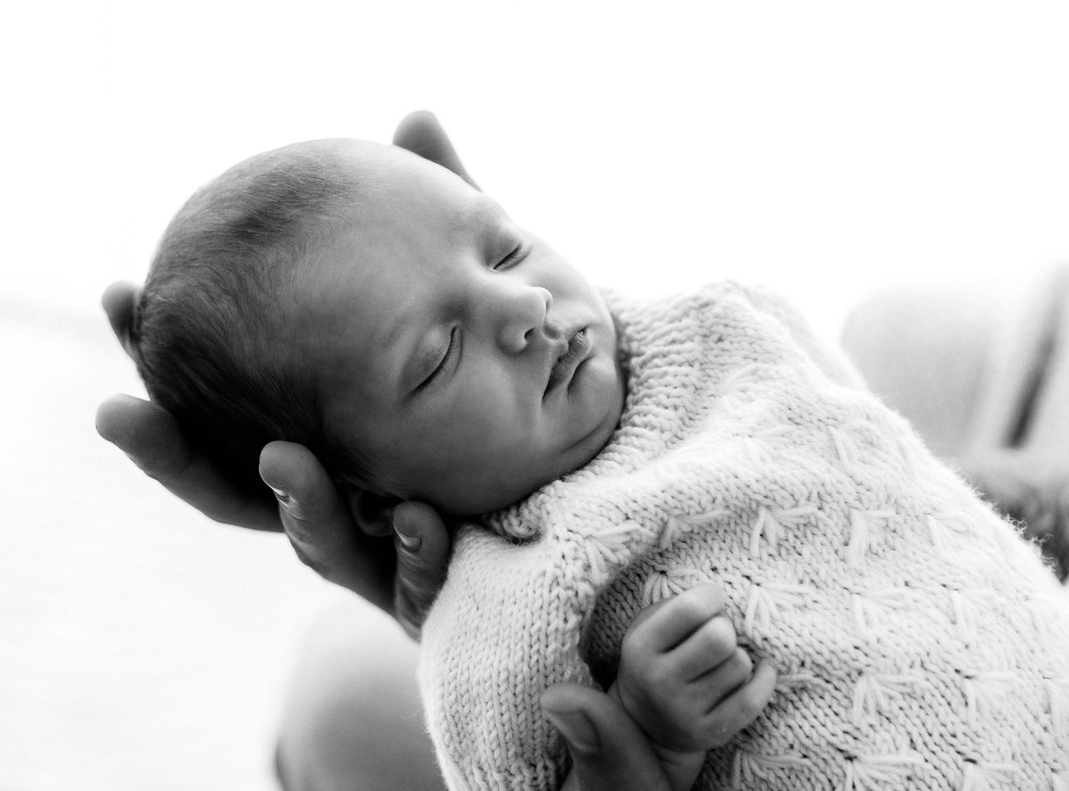 Black and white close-up of a sleeping newborn baby wrapped in a soft knit blanket.