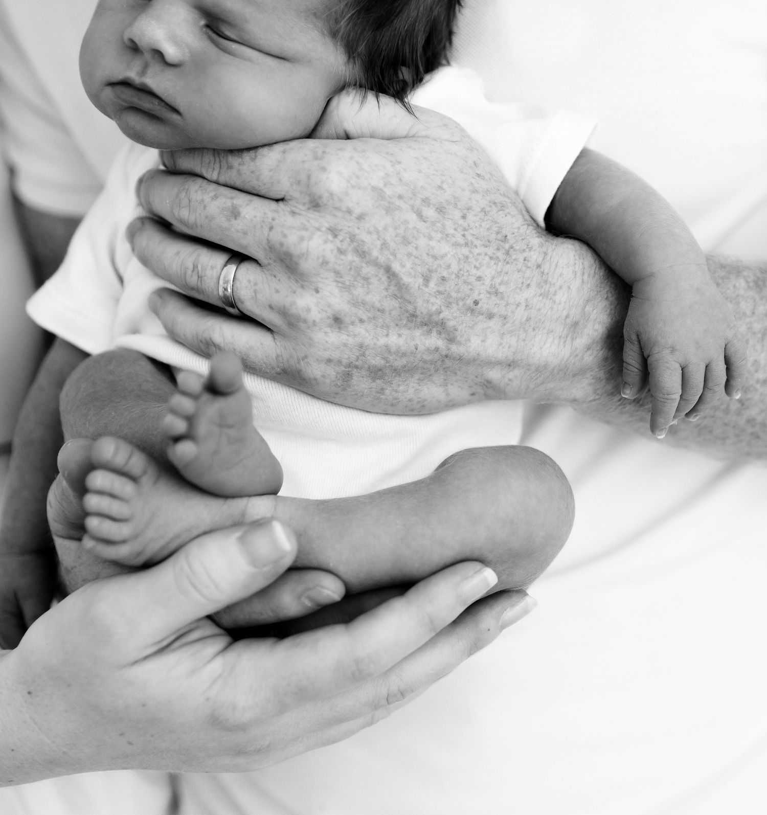 Black and white photo of gentle hands cradling a sleeping newborn's feet.