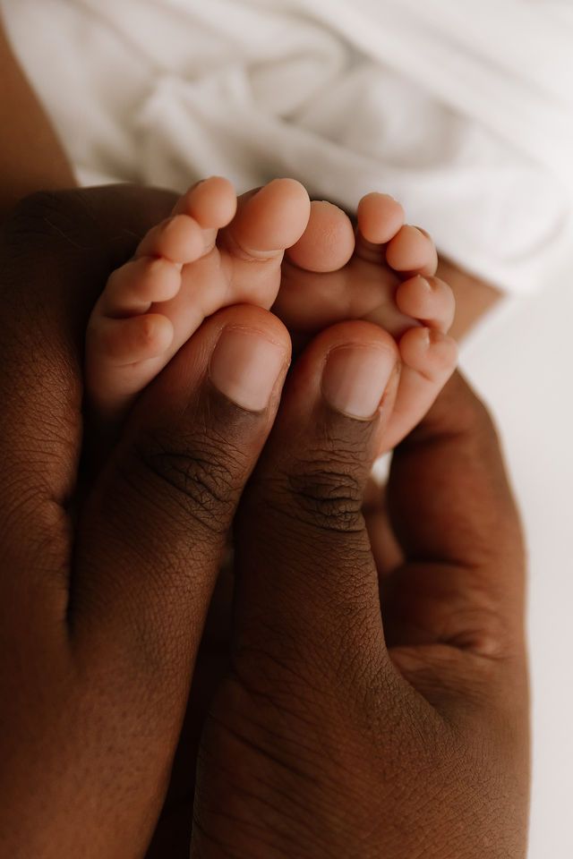 Close-up of a newborn baby's tiny feet resting in an adult's dark-skinned hands, symbolizing love and family.