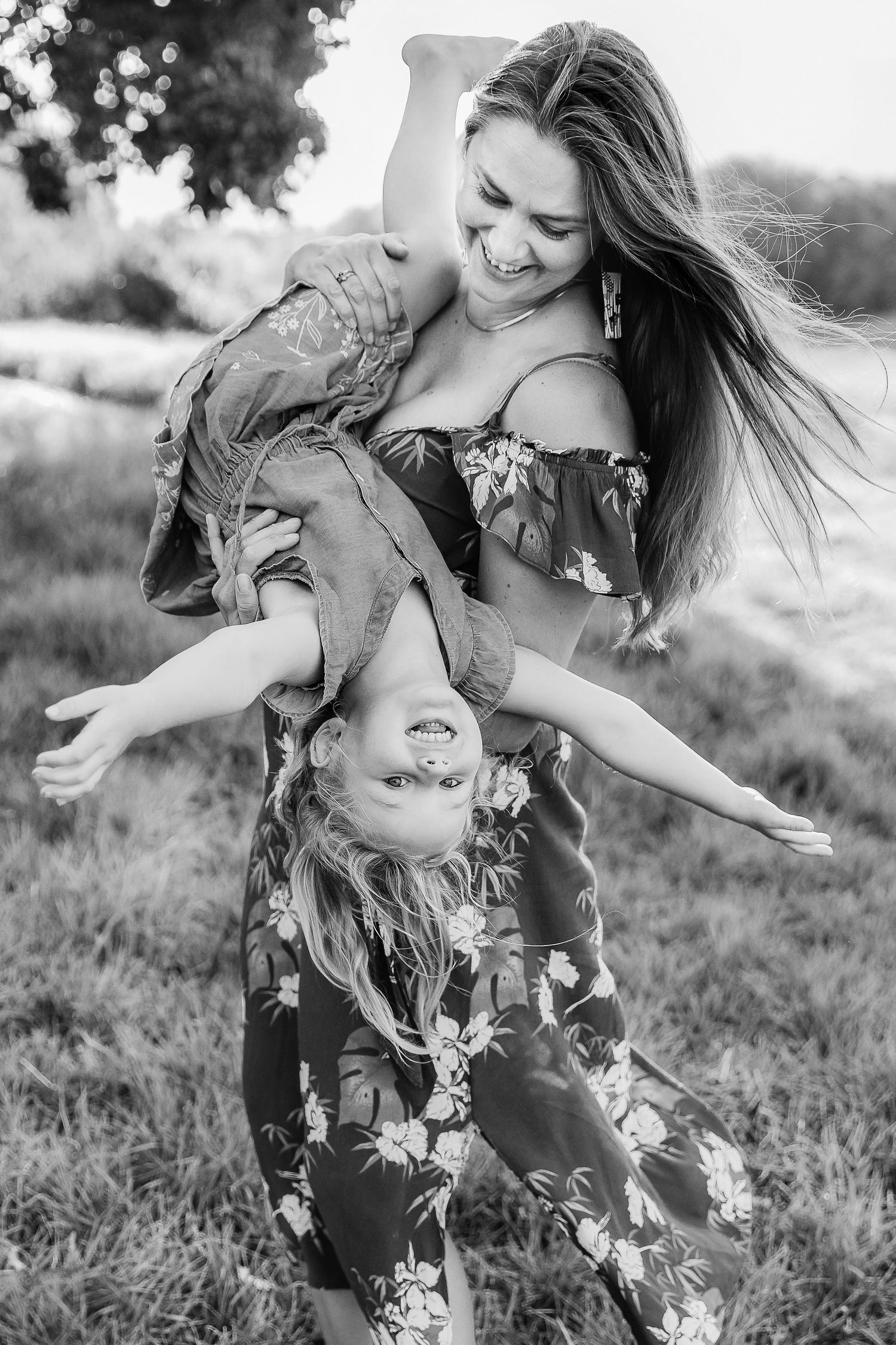 Black and white photo of a mother playfully holding her daughter upside down in a field.