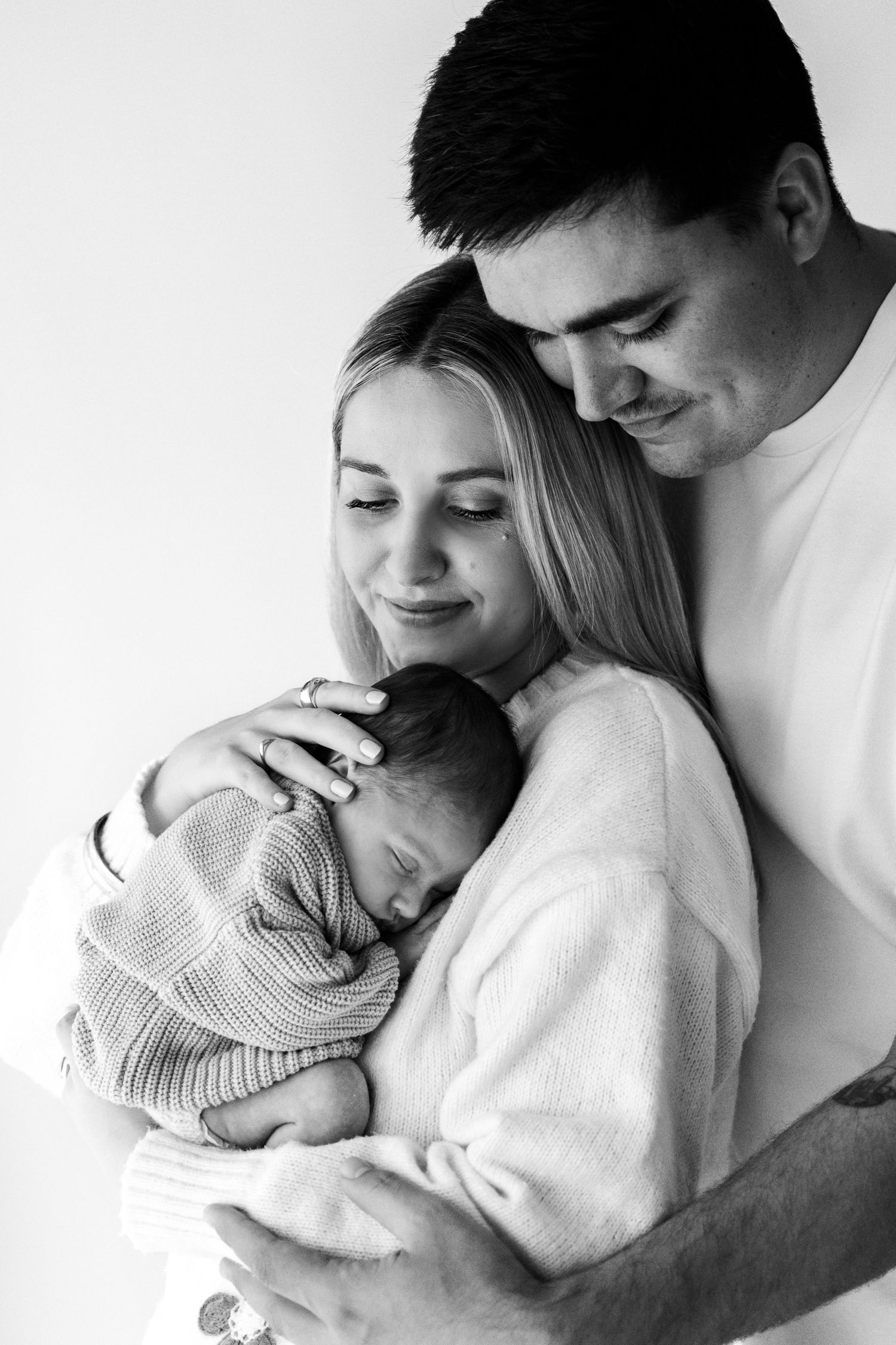 Black and white photo of parents tenderly cradling their sleeping newborn baby, a heartwarming family portrait.