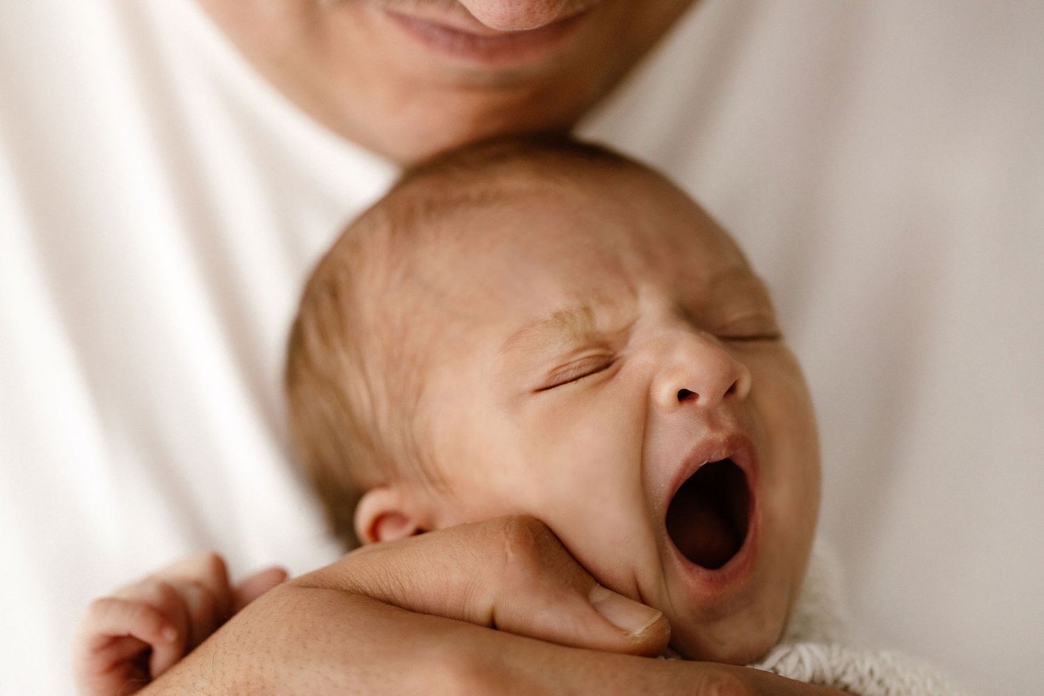 Close-up of yawning newborn baby held gently in parent's hands.