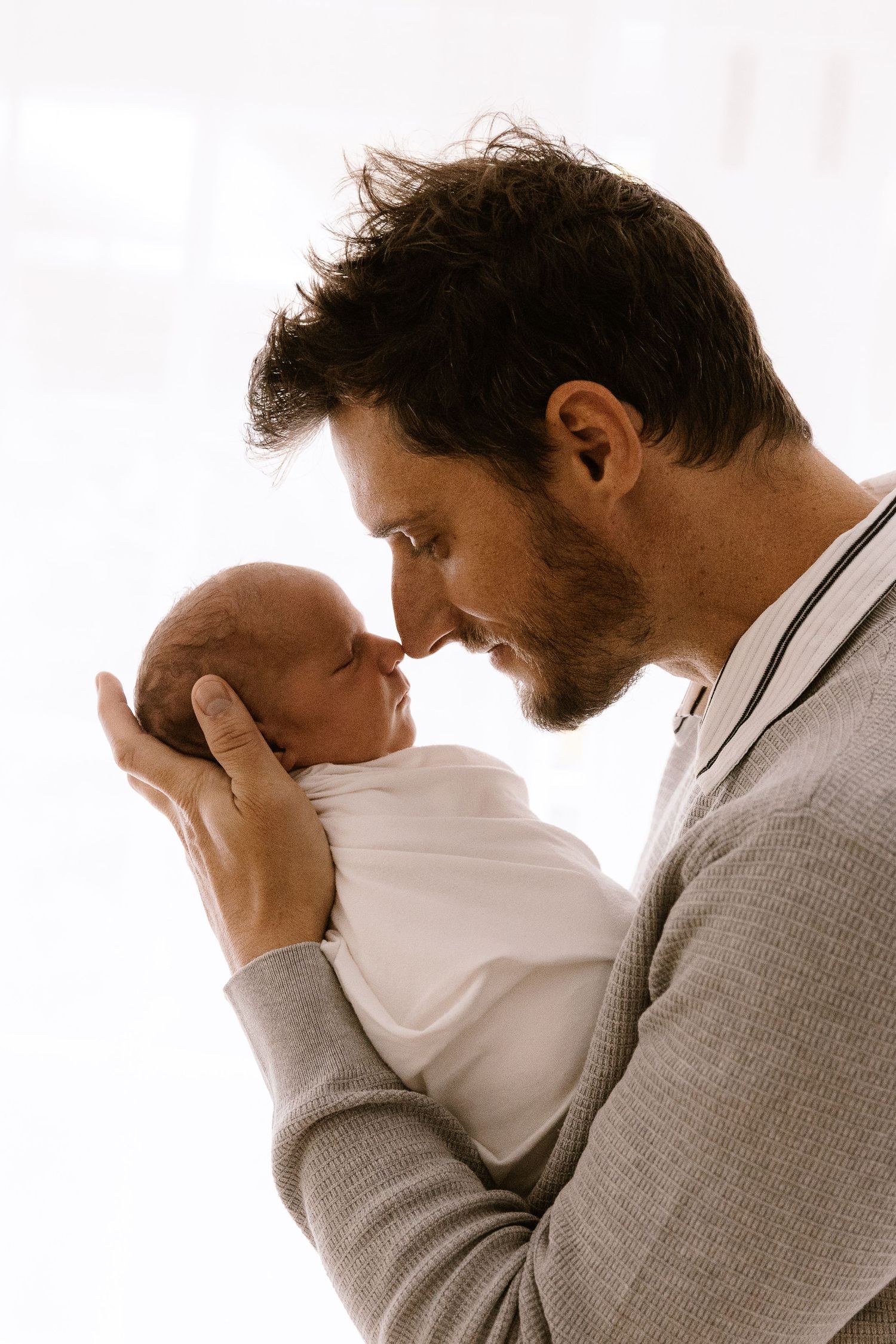 A loving father tenderly holds his newborn baby close, touching noses in an intimate bonding moment.