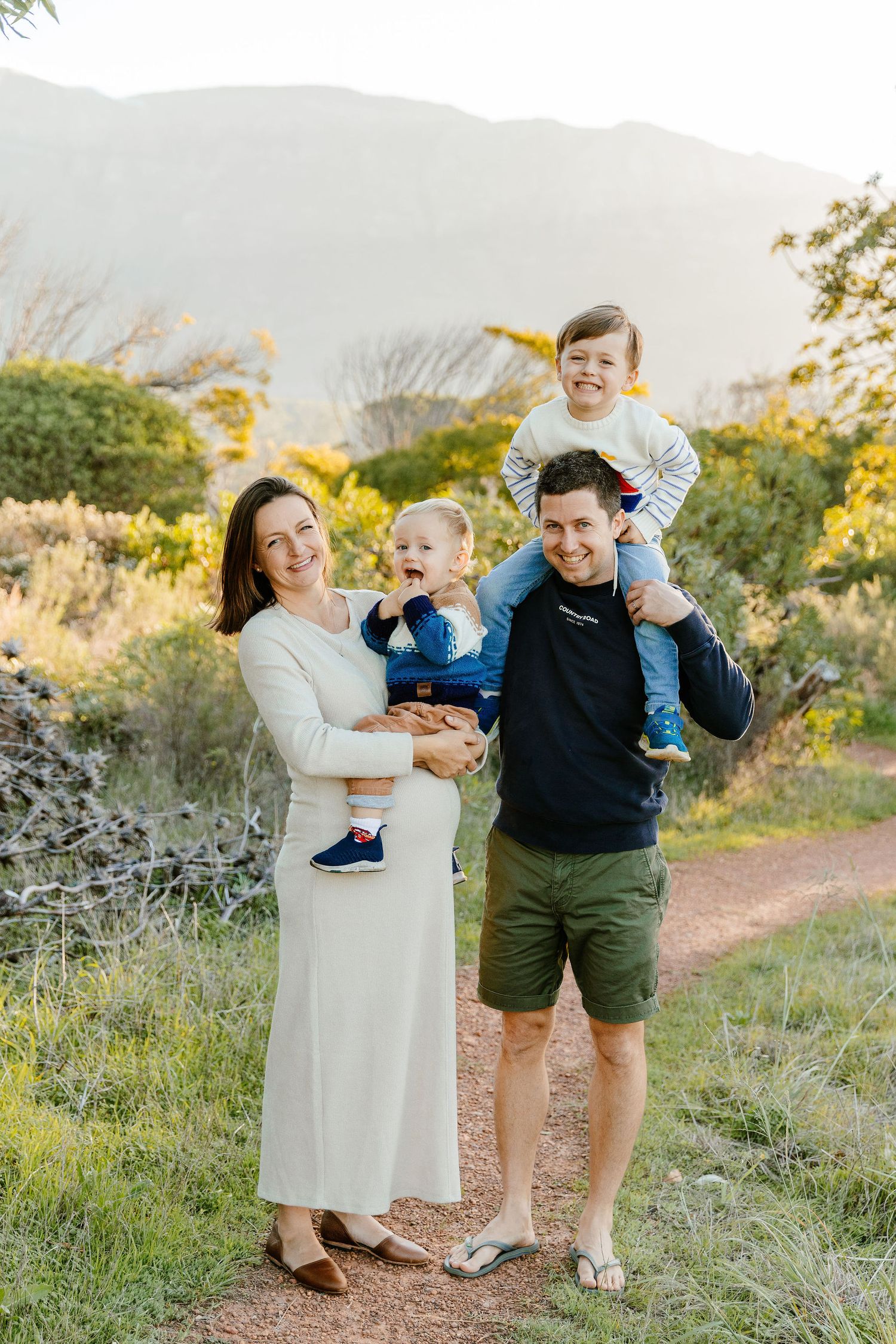 Happy family of four poses on a nature trail at golden hour with mountains in background.