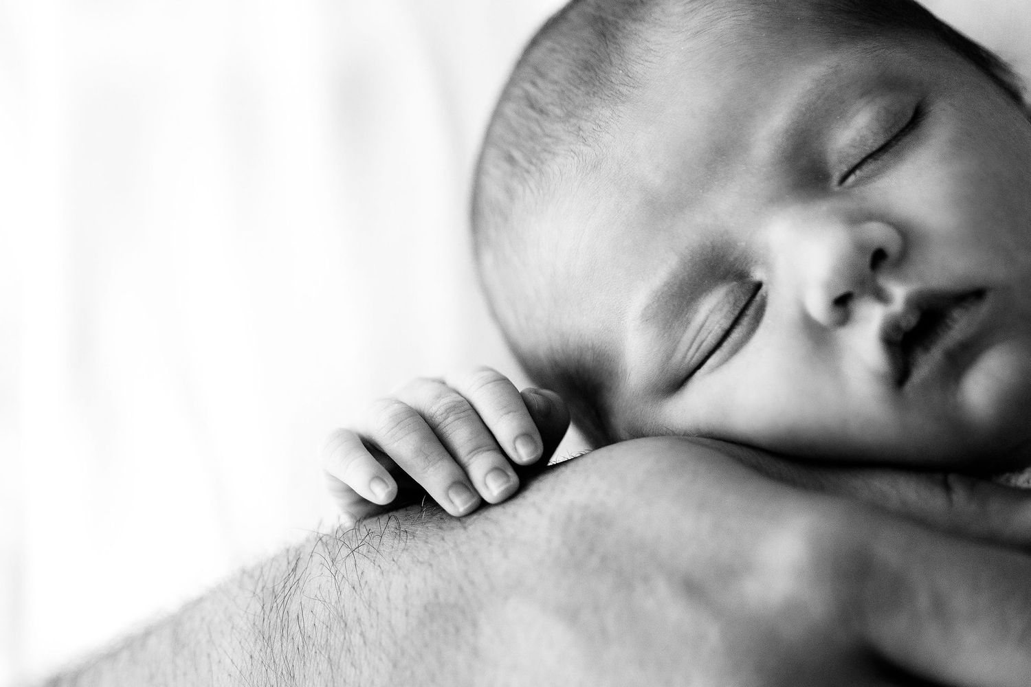 Black and white photo of a sleeping newborn baby resting peacefully on an adult's arm.