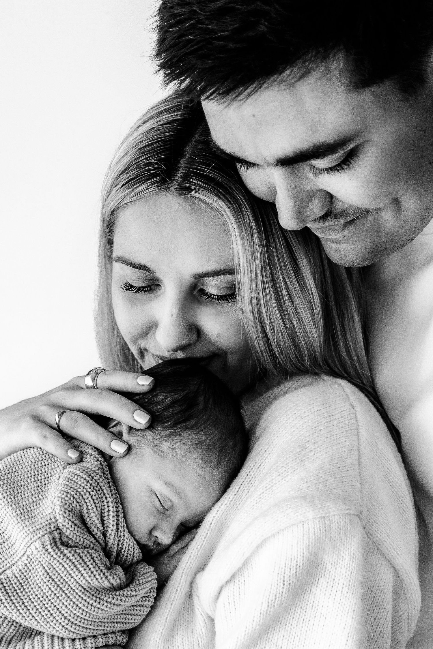 Black and white photo of parents lovingly holding their sleeping newborn baby.