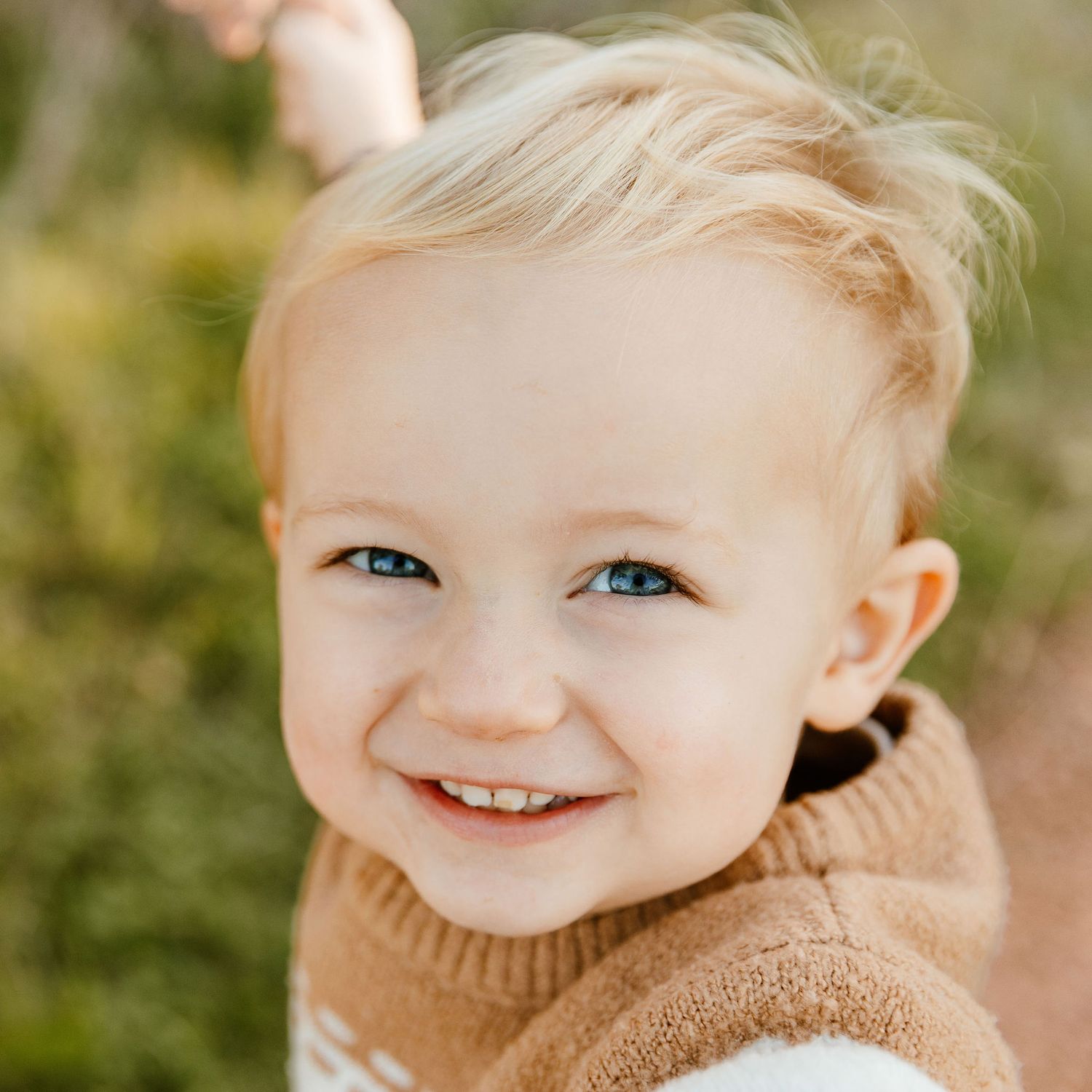 Close-up portrait of a happy blonde toddler with blue eyes smiling outdoors.