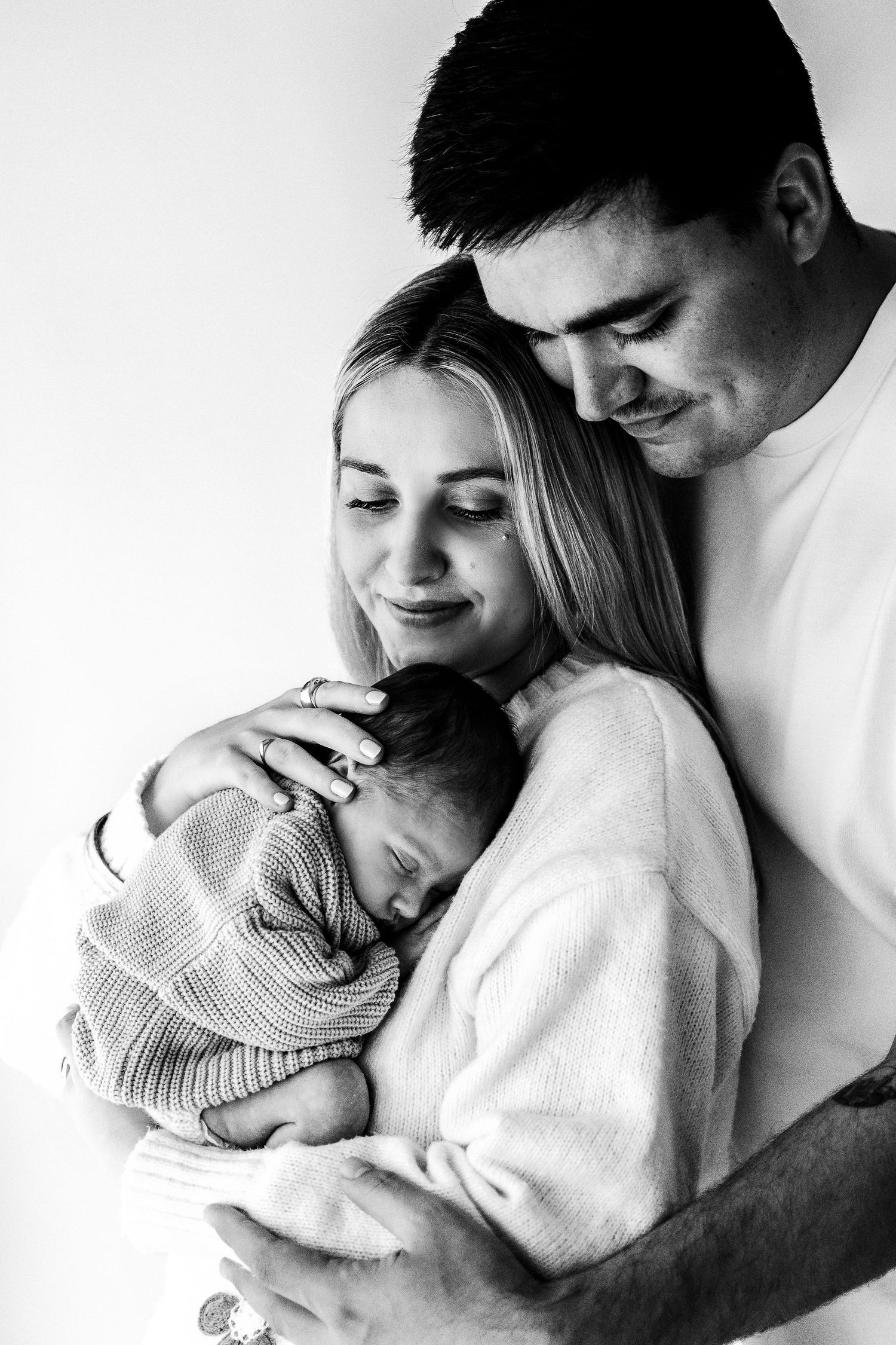 Black and white image of loving parents cradling their sleeping newborn baby.