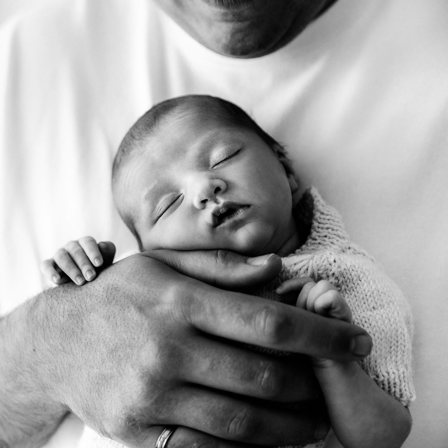 Close-up black and white photo of sleeping newborn baby cradled in fathers arms.