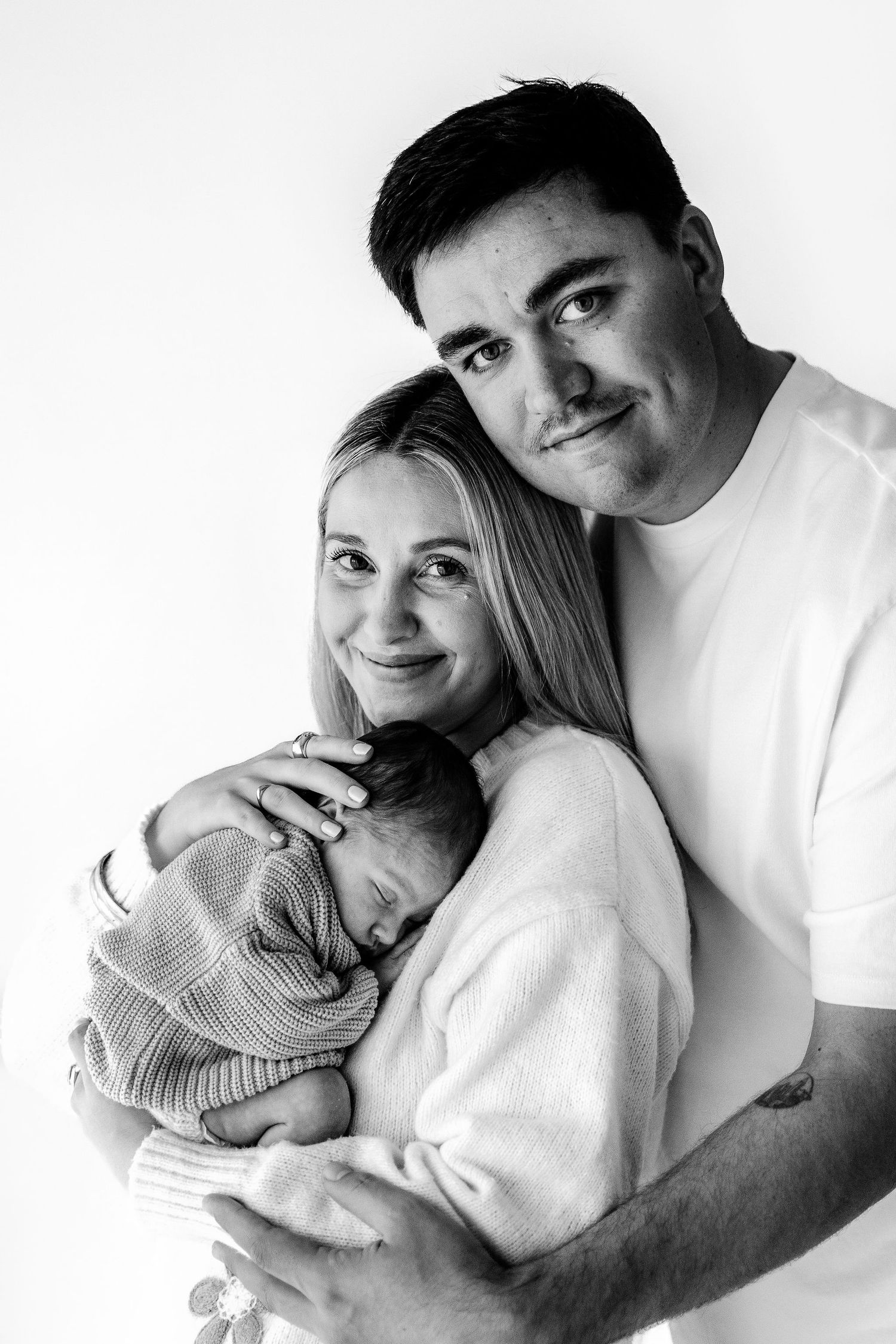 Black and white portrait of smiling parents holding their sleeping newborn baby.