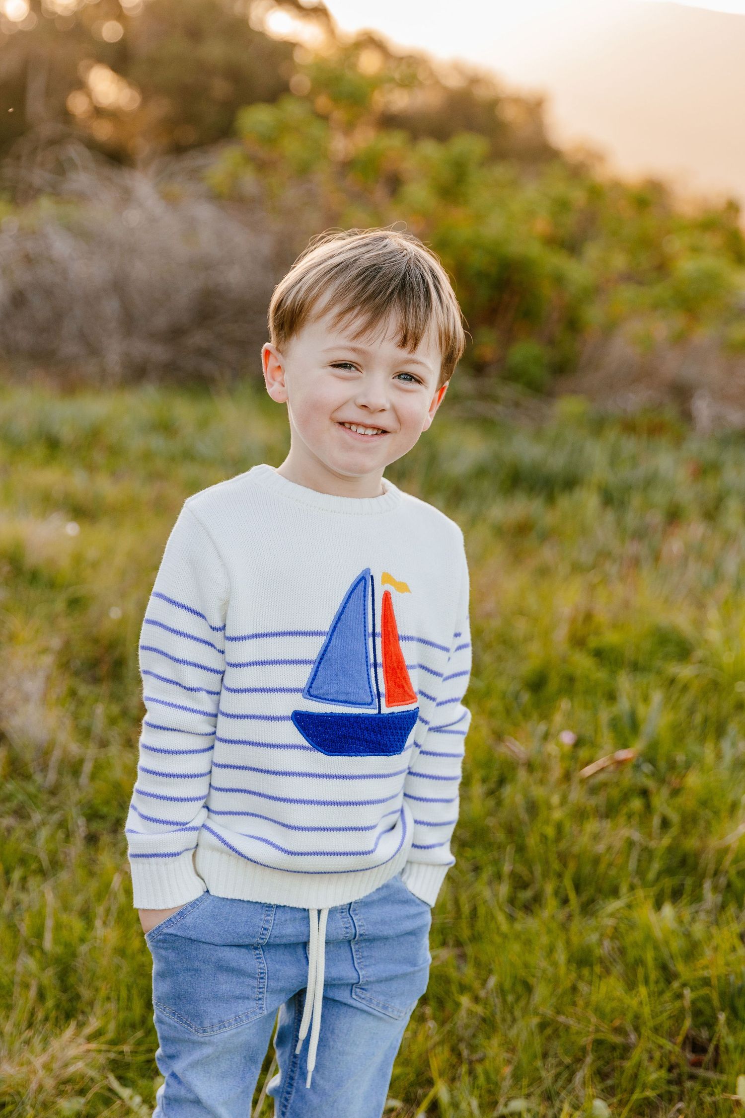 Happy young boy in a striped sailboat sweater laughing in a golden sunlit field.