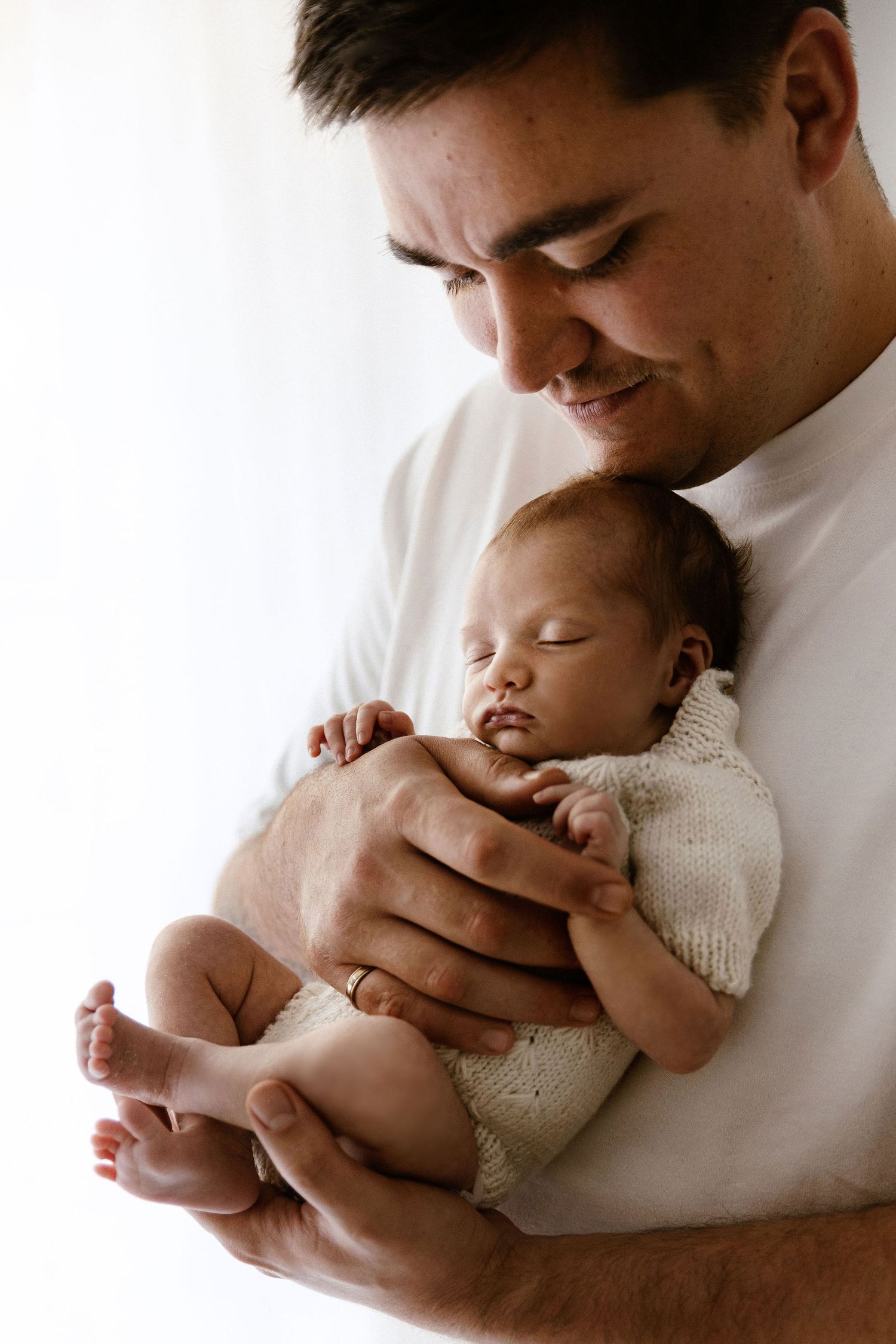 Proud father gently holds sleeping newborn baby close to his chest in portrait.