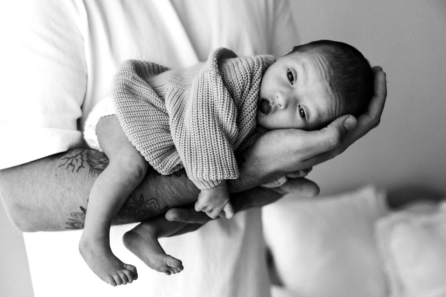 Black and white photo of father holding alert newborn baby in one hand.