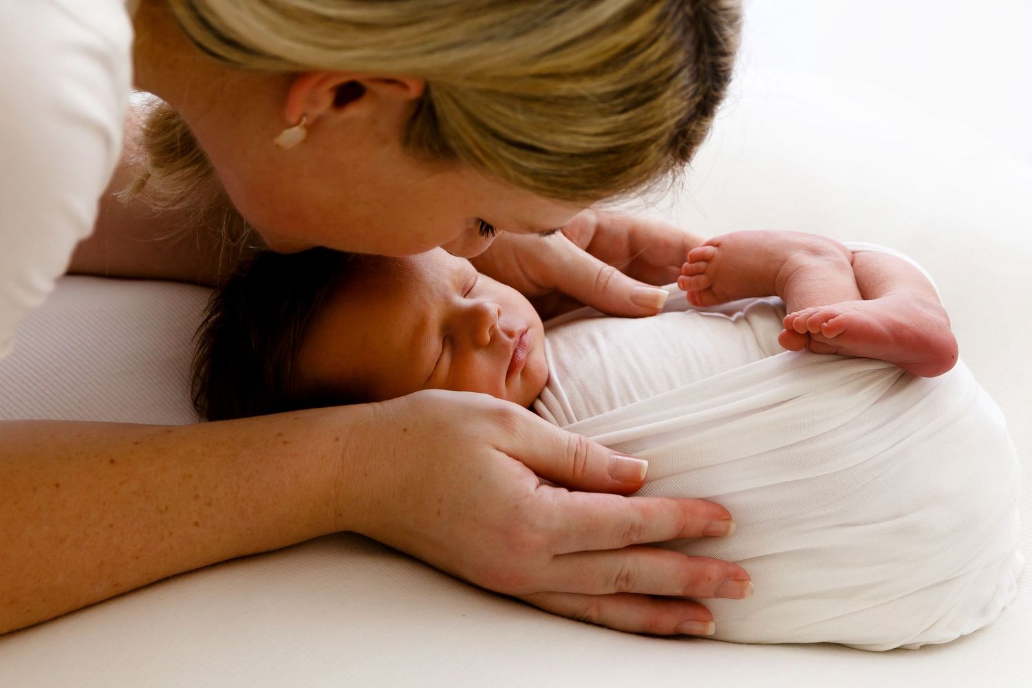 A tender moment showing a parent cuddling close to a sleeping newborn baby on white bedding.