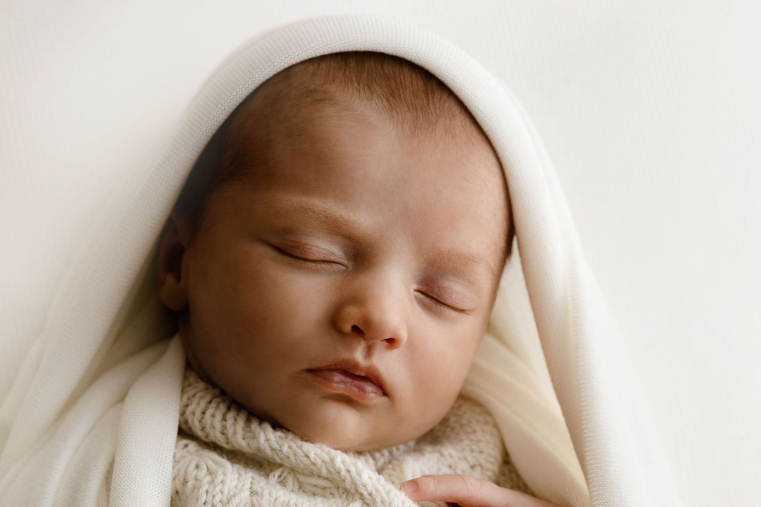 Serene newborn baby sleeping soundly wrapped in a cream white blanket in a soft light studio photo.