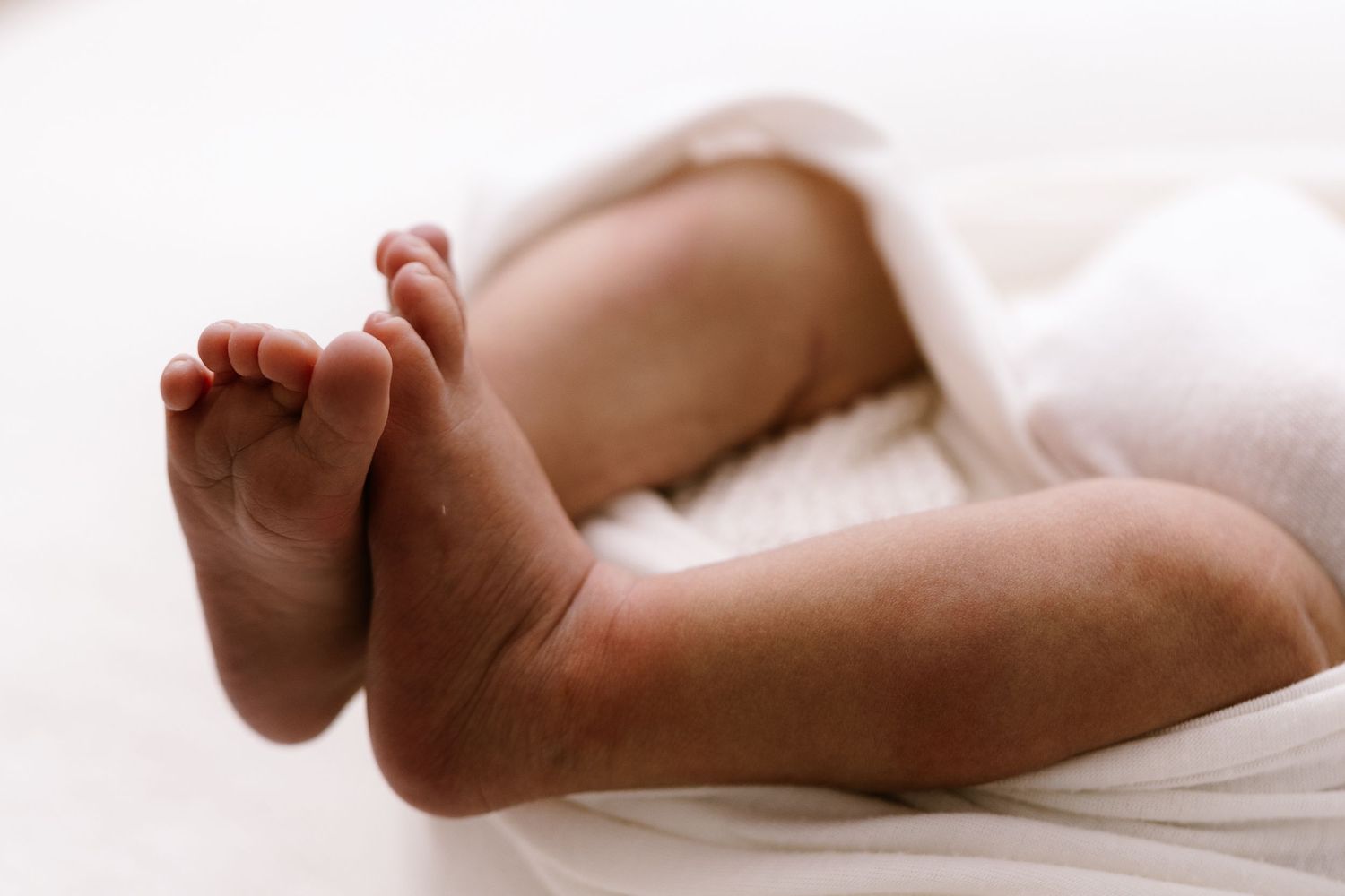 Close-up of a newborn baby's tiny feet and legs wrapped in a soft white blanket.