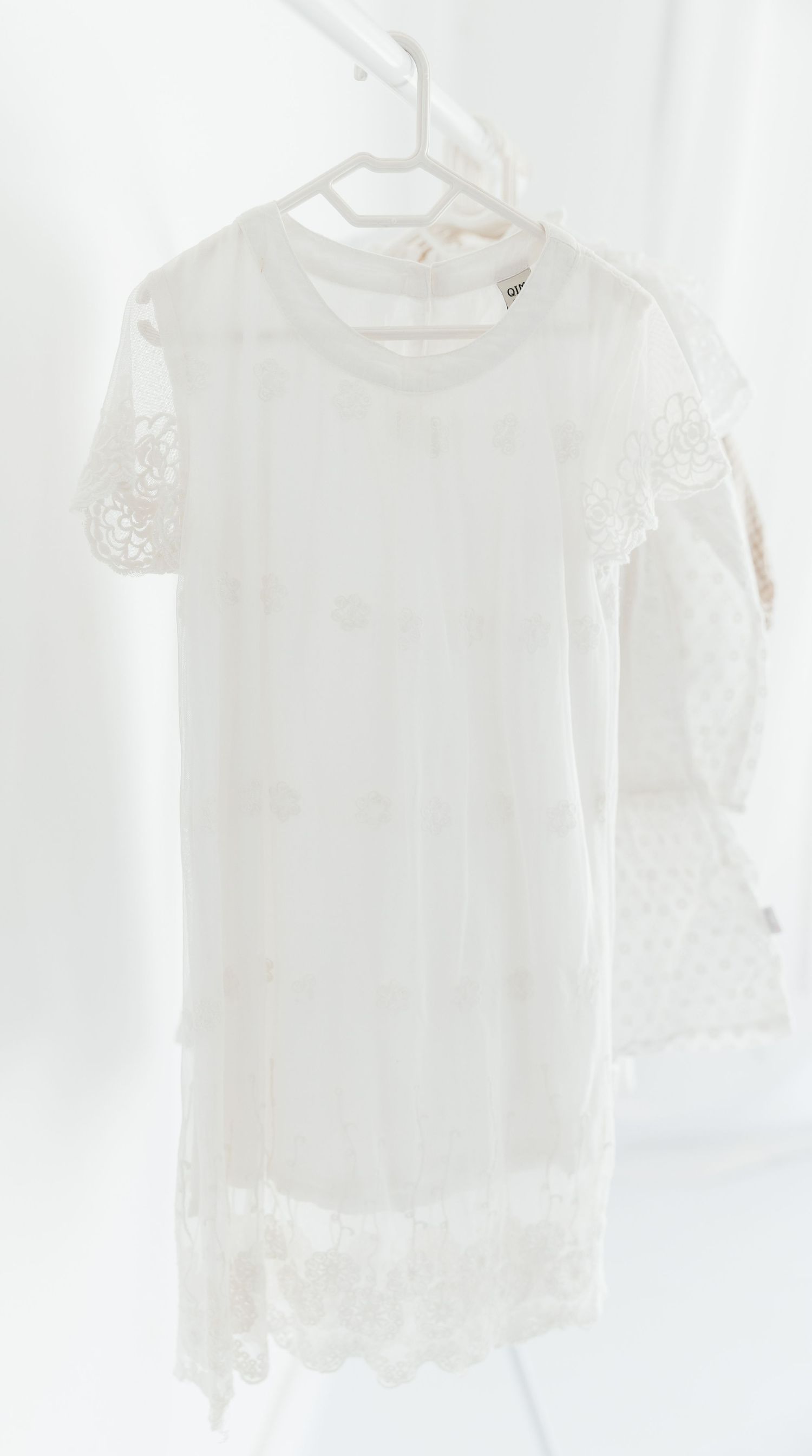White lace mini dress with floral embroidery and scalloped hem, displayed on a hanger against a white background.