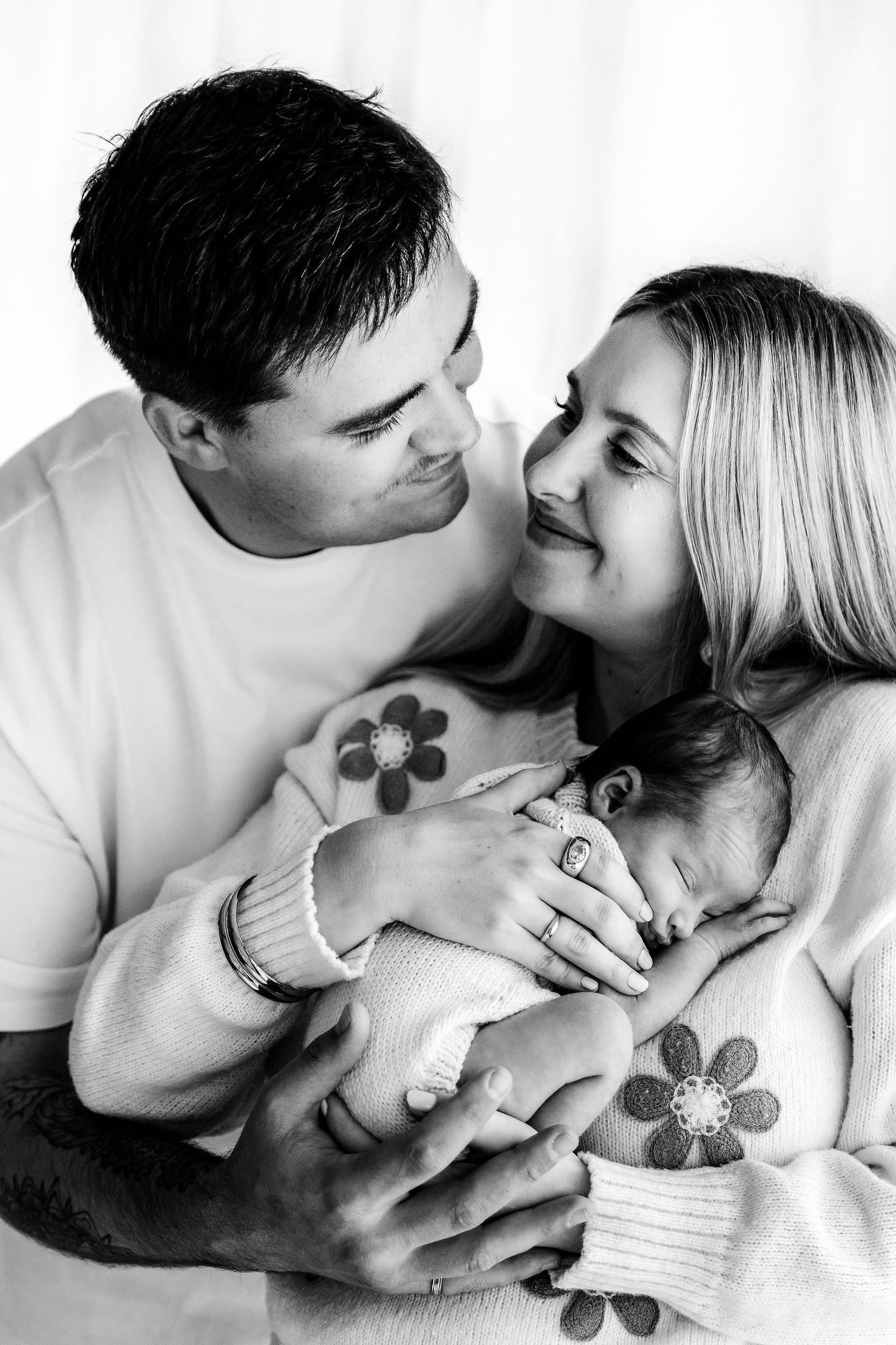 Black and white portrait of smiling parents lovingly holding their sleeping newborn baby together.