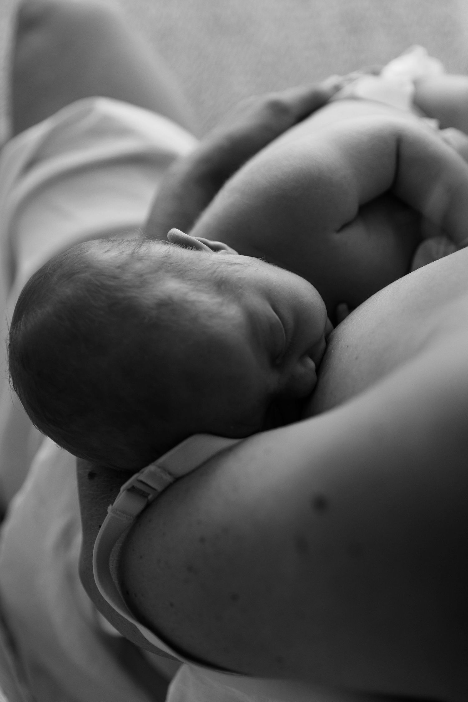 Black and white photo of a newborn baby being cradled in a mother's arms while breastfeeding.