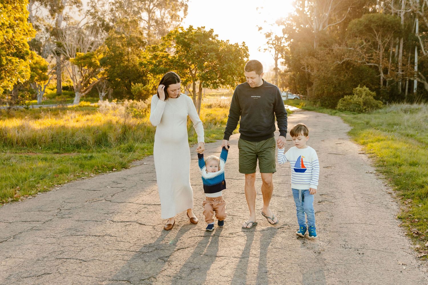 Family of four strolling together on a sunlit path surrounded by greenery.