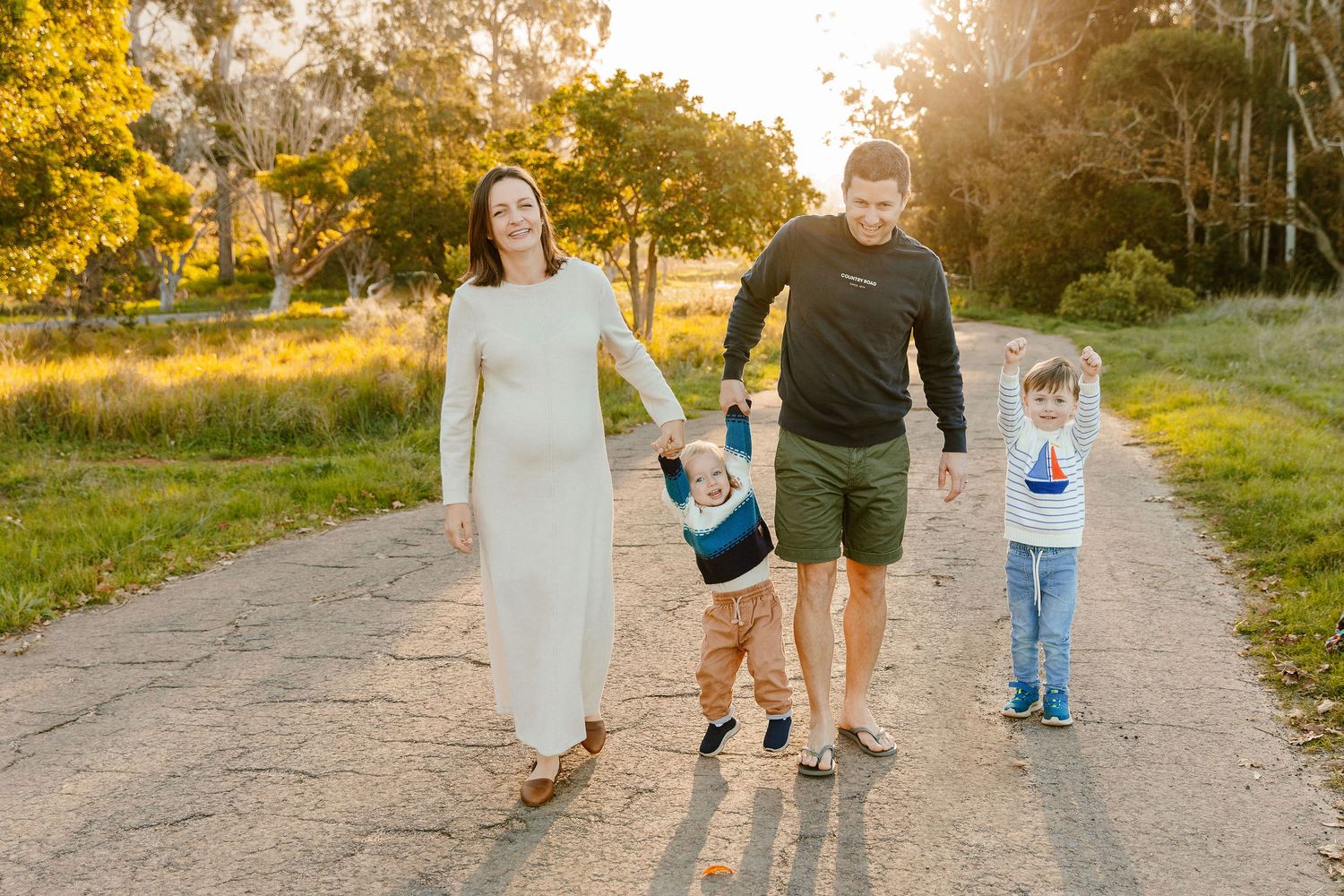 Happy family of four walking together on a sunny dirt road outdoors.