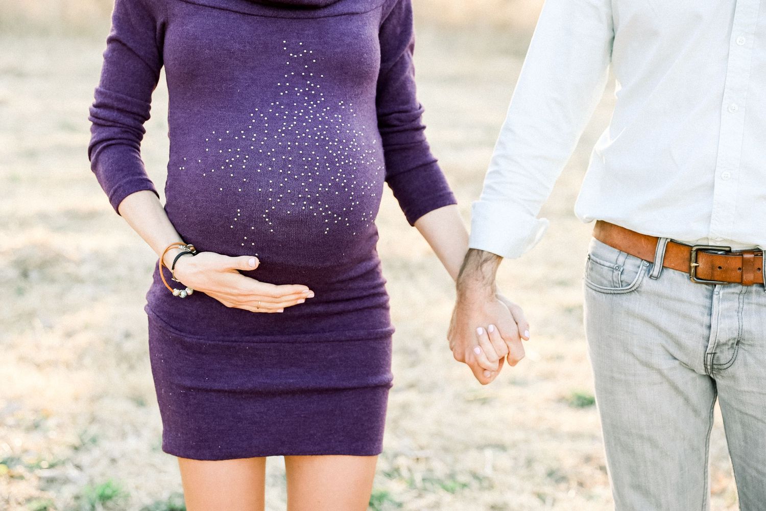 Close-up of a sparkly purple maternity dress with hands cradling the baby bump outdoors.