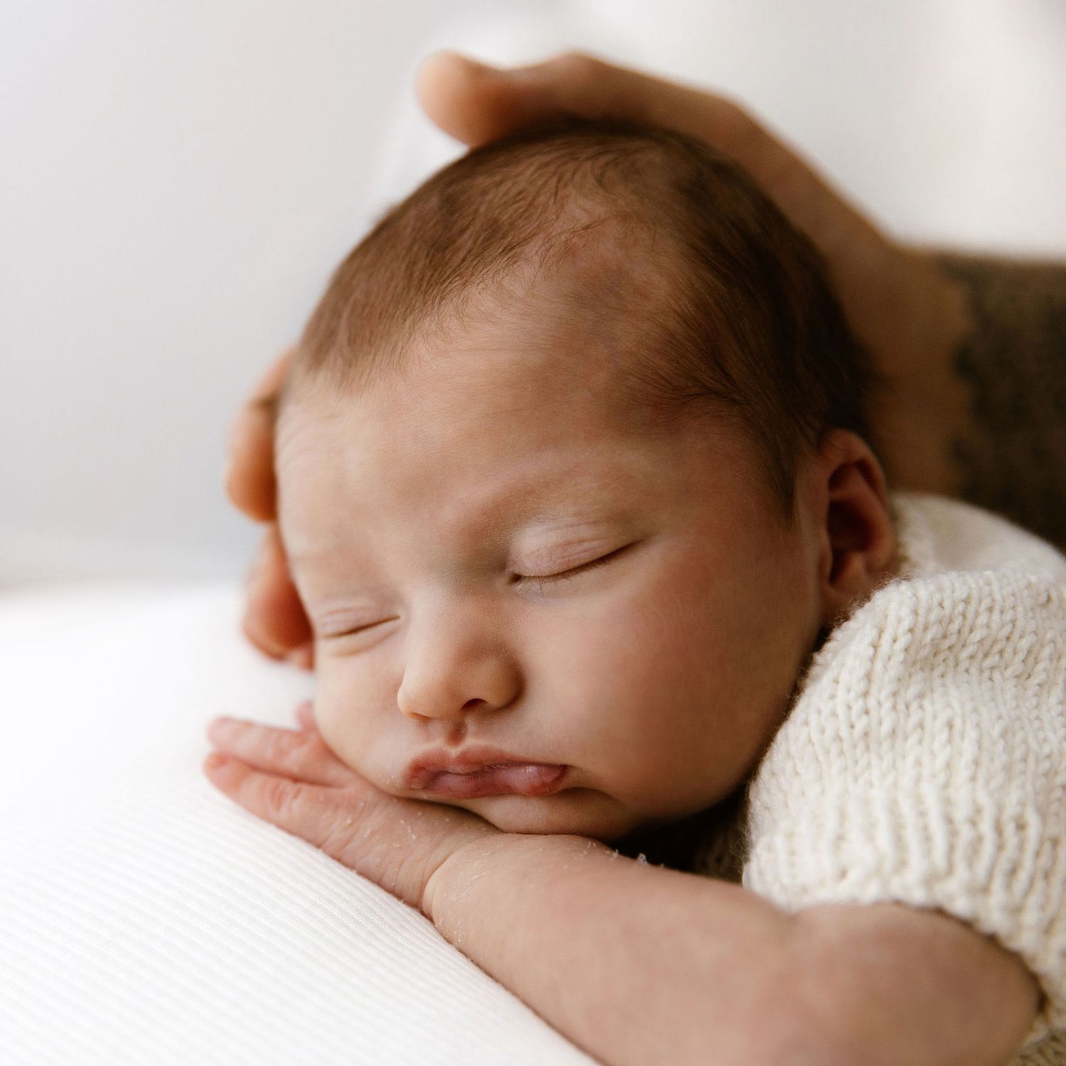 Color close-up of a peaceful sleeping newborn baby resting on hands with a parent's hand on head.