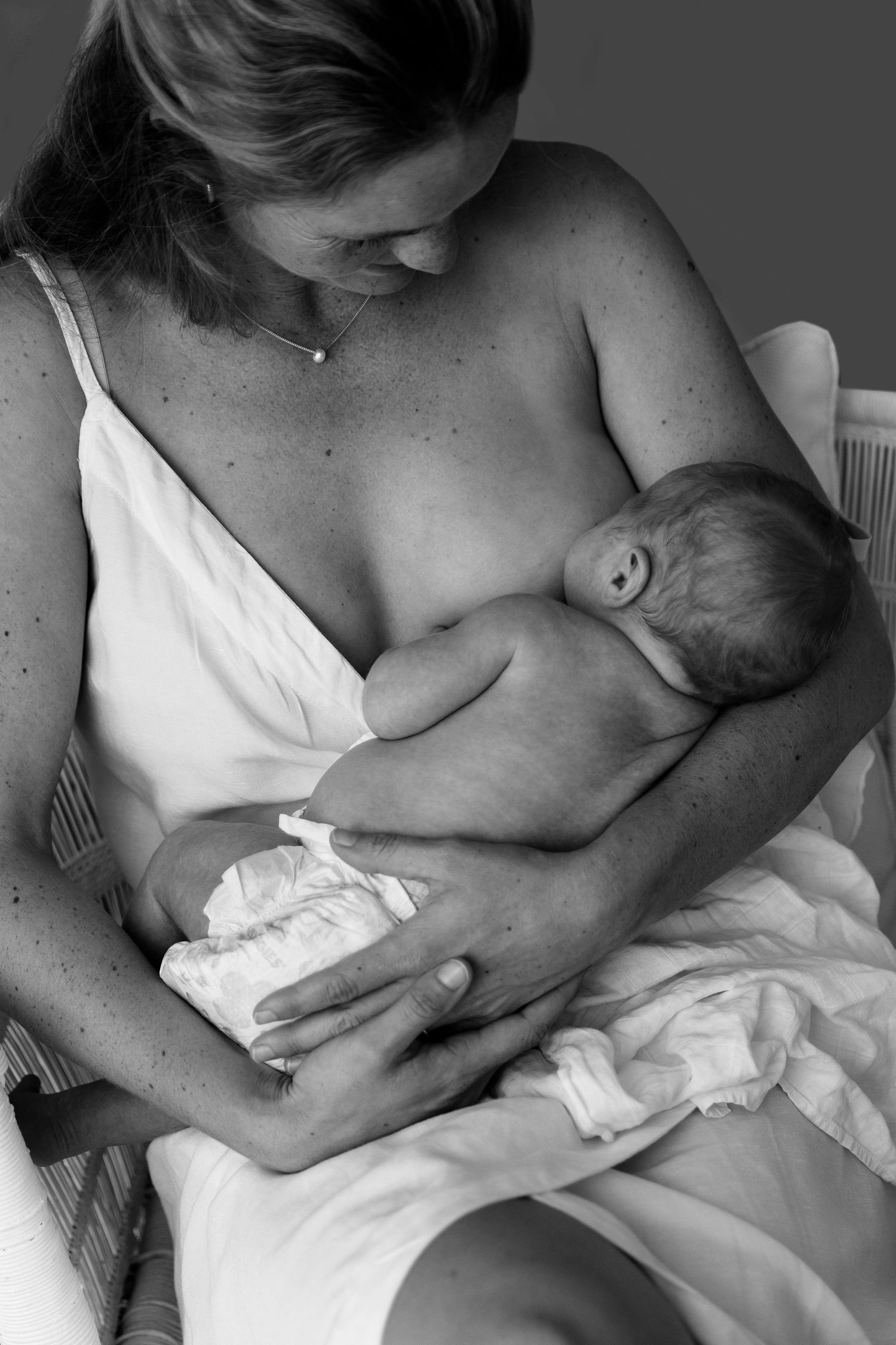 Black and white photo of a mother tenderly breastfeeding her newborn baby while seated in a chair.