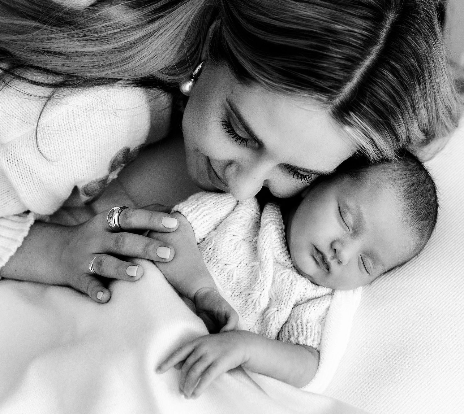 Black and white photo of mother tenderly kissing her sleeping newborn baby.