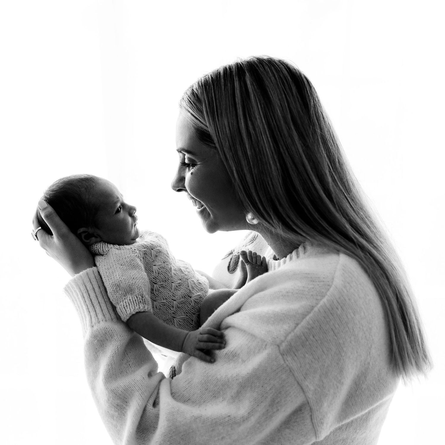 Black and white photo of a smiling mother holding her newborn baby up close in a bright studio.