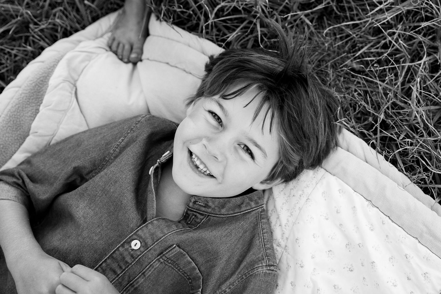 Black and white photo of a happy young child lying on a blanket in grass, smiling joyfully at the camera.