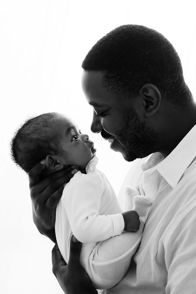 Black and white photo of a smiling father holding his newborn baby face to face in a tender moment.