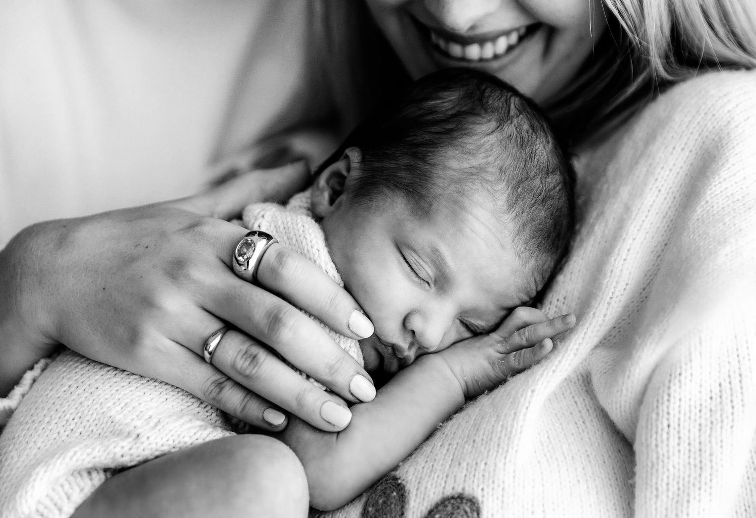 Black and white photo of a mother cradling her sleeping newborn baby close to her chest with gentle hands.