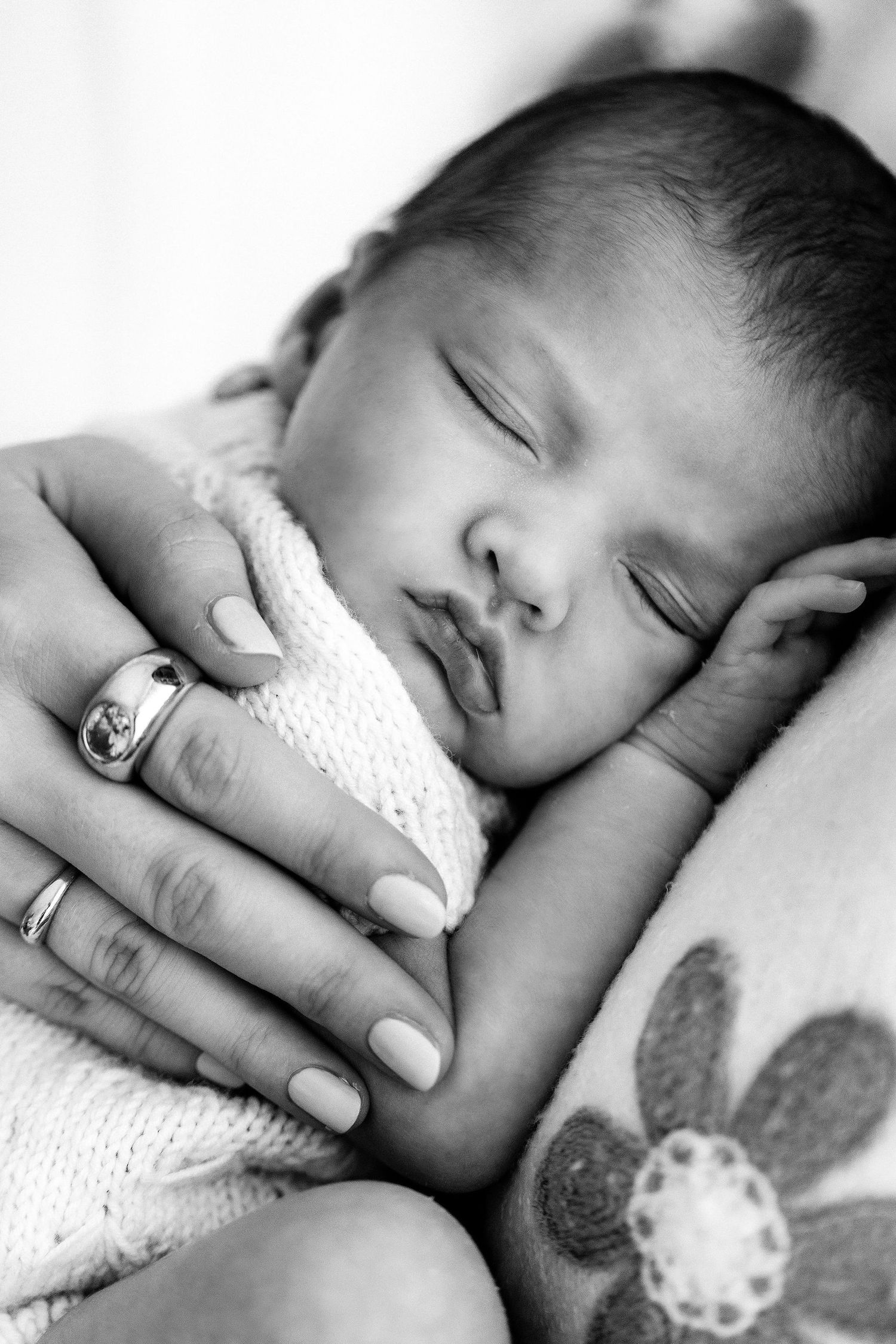 Black and white photo of a sleeping newborn baby cradled in a mother's hands wearing rings.