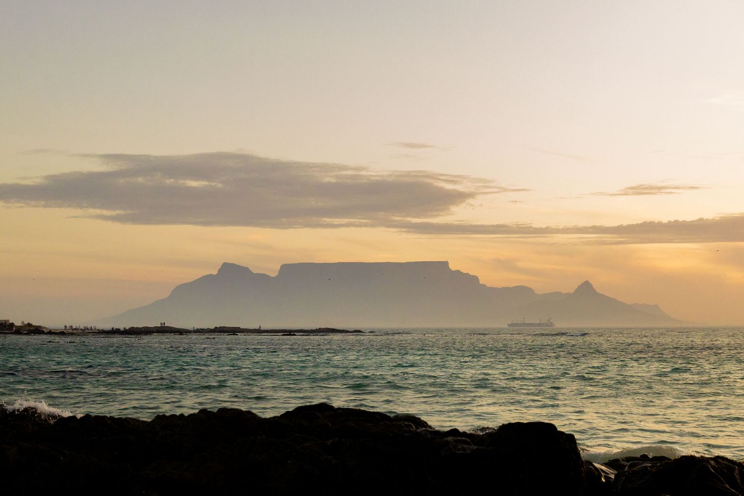 Table Mountain silhouetted against a golden sunset sky over calm ocean waters in Cape Town, South Africa.