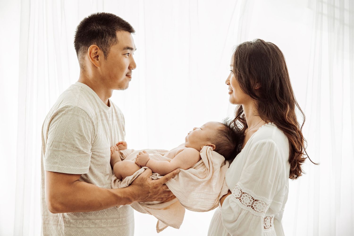 Parents holding their newborn baby near a window, lifestyle newborn photography Sydney