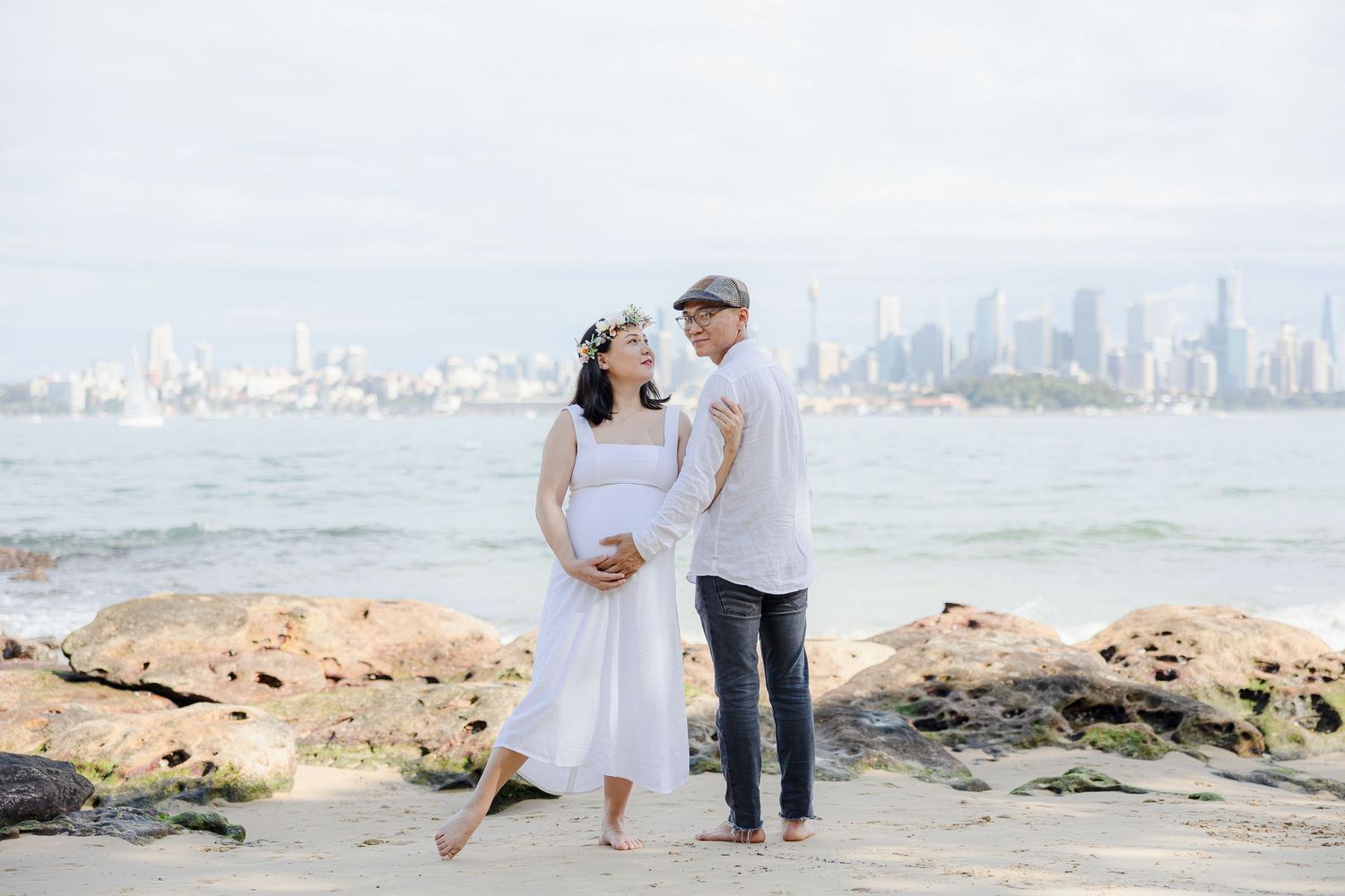 Couple maternity portrait at rocky beach with city skyline, Sydney maternity photographer