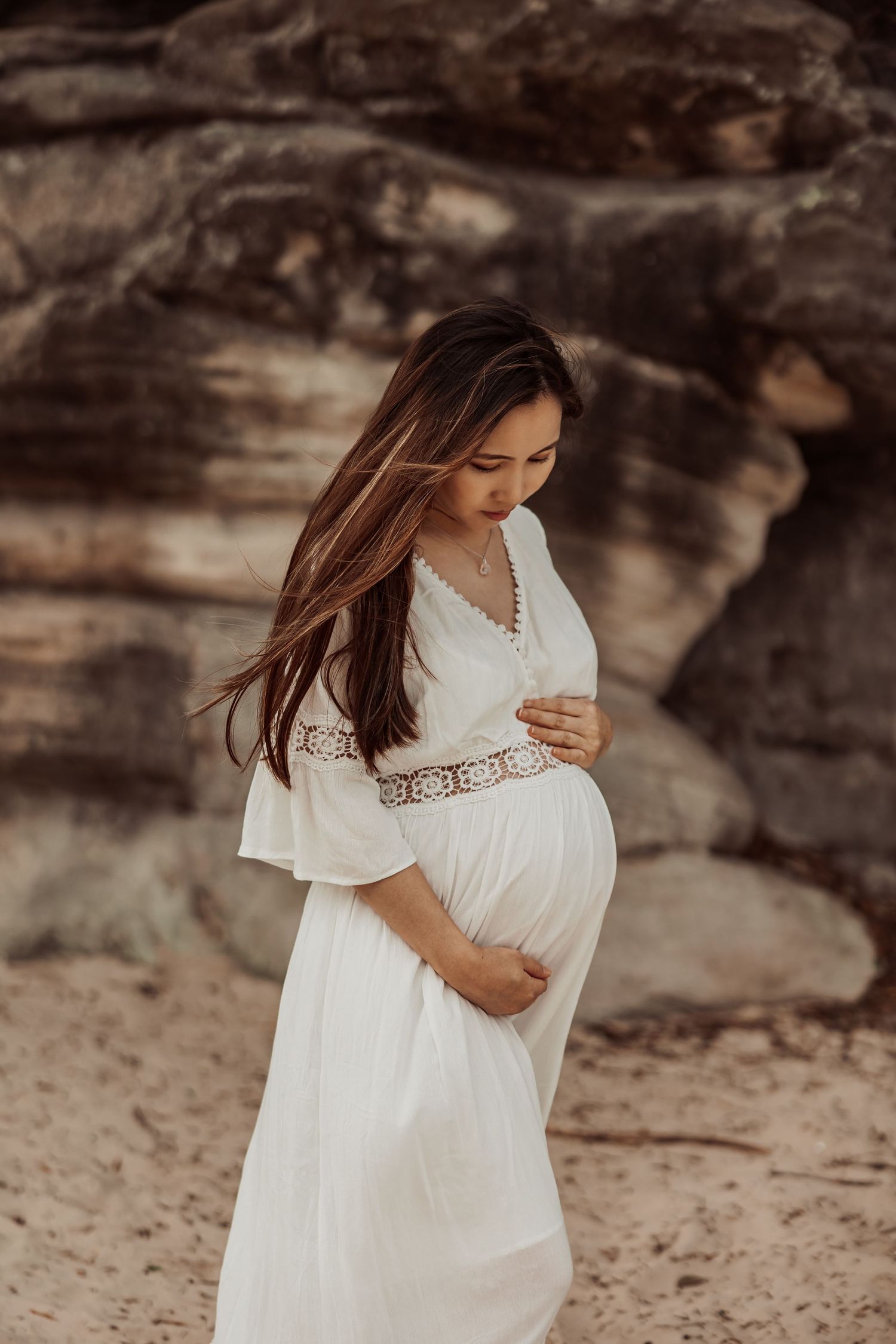 Outdoor maternity portrait of pregnant woman in a white dress near rocks, Sydney maternity photographer