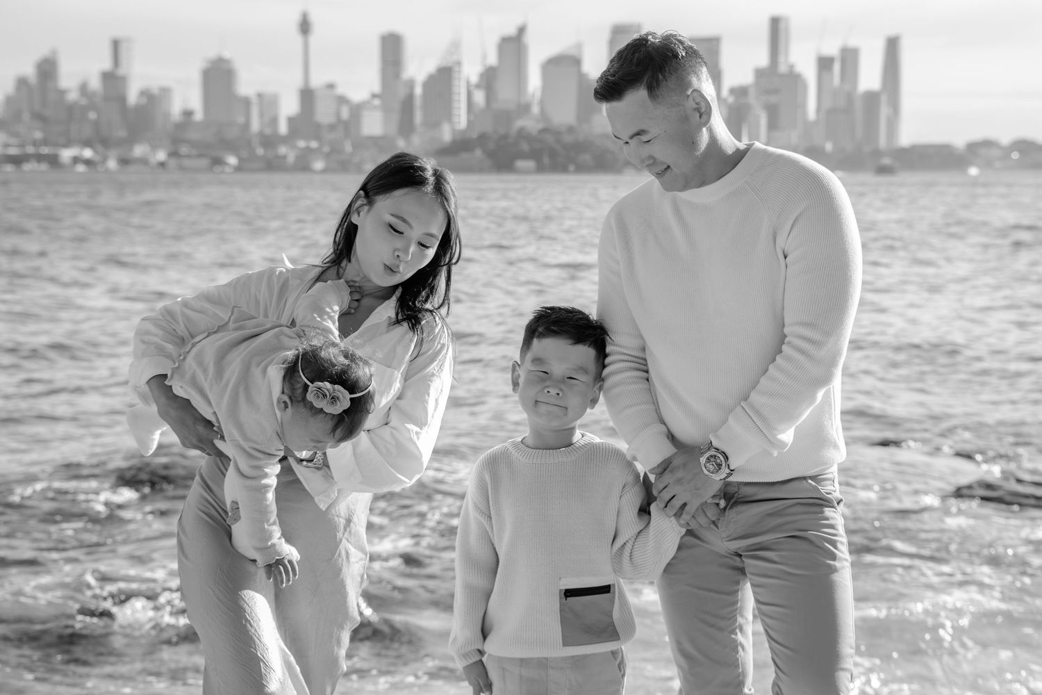 Black and white family portrait by the water with Sydney skyline, Sydney family photographer