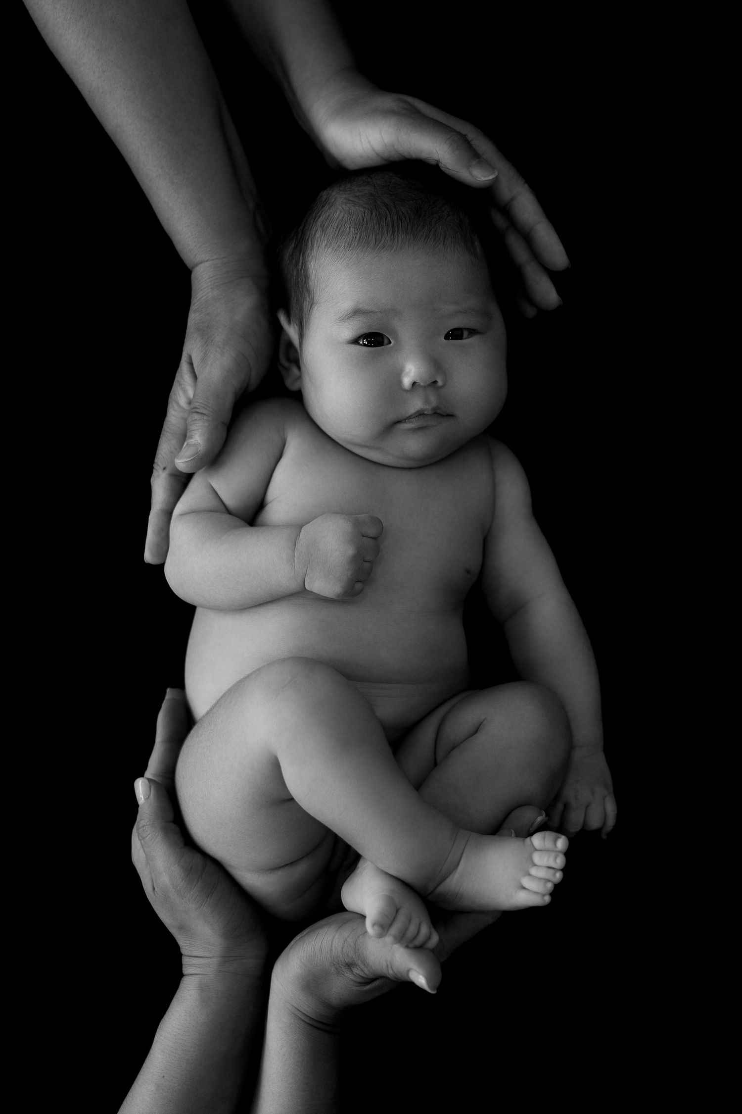 Black and white newborn photo of baby held gently in parents’ hands, Sydney newborn photography