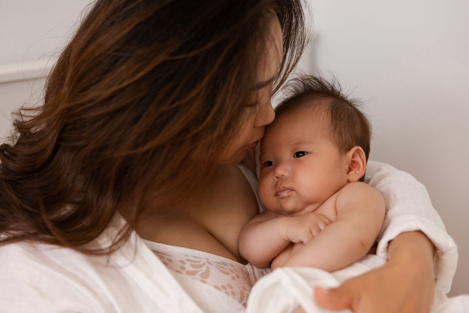 Mother holding newborn baby close in soft natural light, at home newborn session Sydney