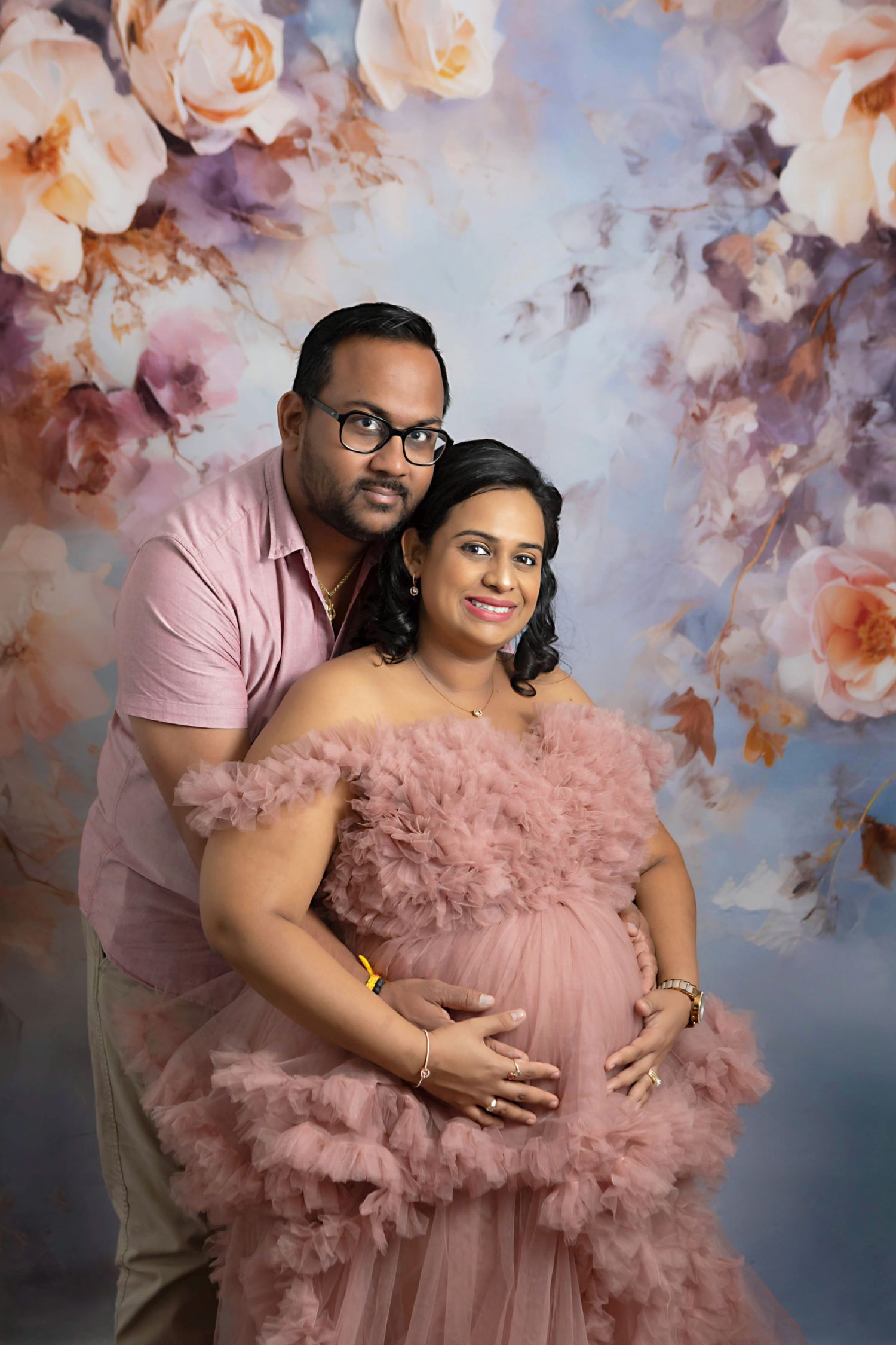 Girl mom in pink poofy dress posing with her spouse in front of a blue floral backdrop
