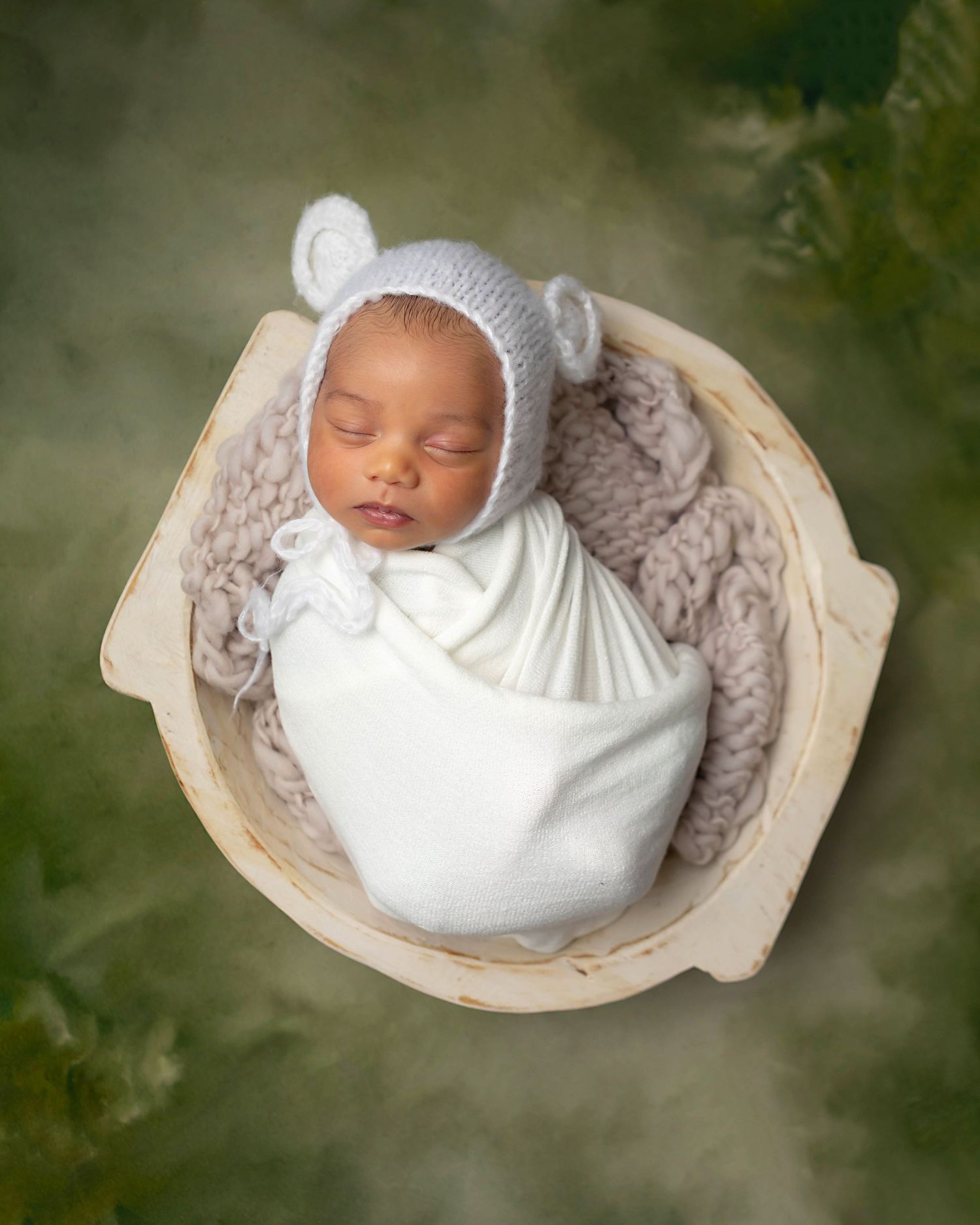 Newborn baby wearing a white bear hat and swaddled in a white bowl