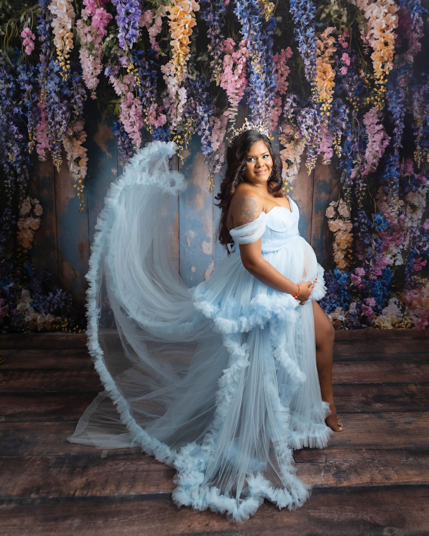 Boy mom styled in blue posing with a heavily decorated floral backdrop