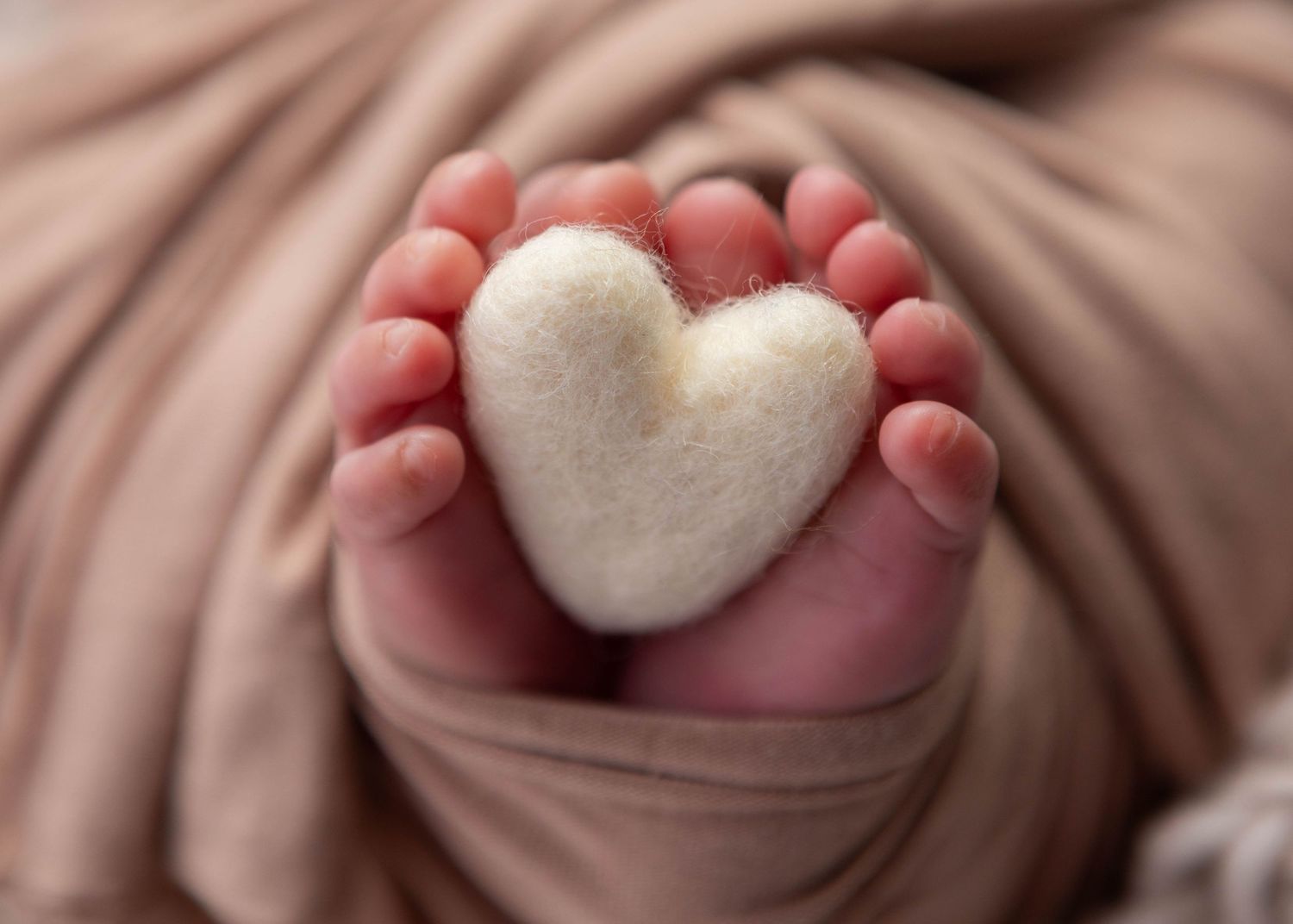 baby toes holding felted white heart.