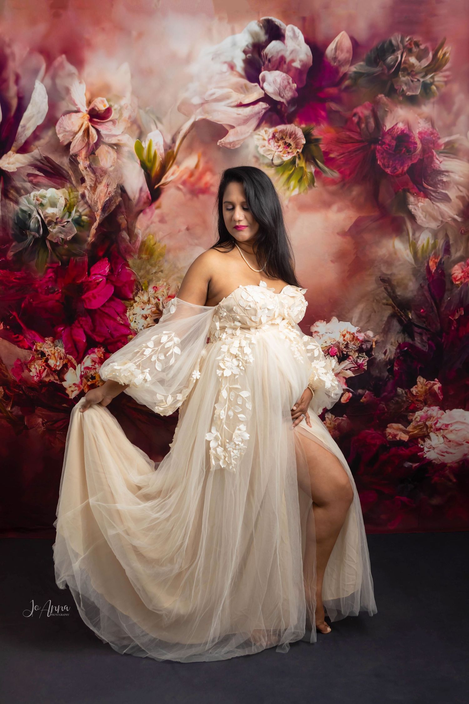 Pregnant mom styled in beige with a vibrant red and magenta floral backdrop