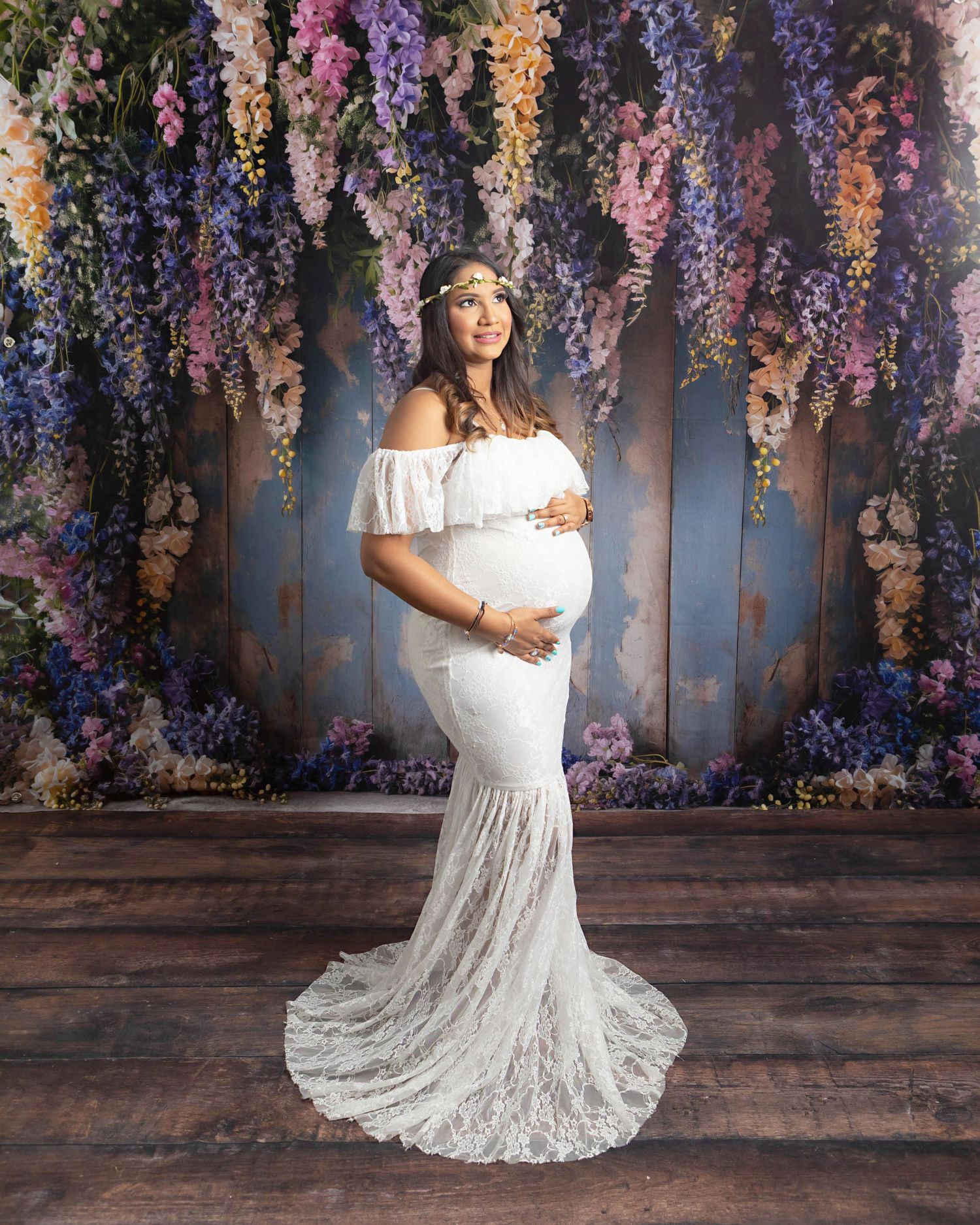 Boy mom styled in white posing with a heavily decorated floral backdrop