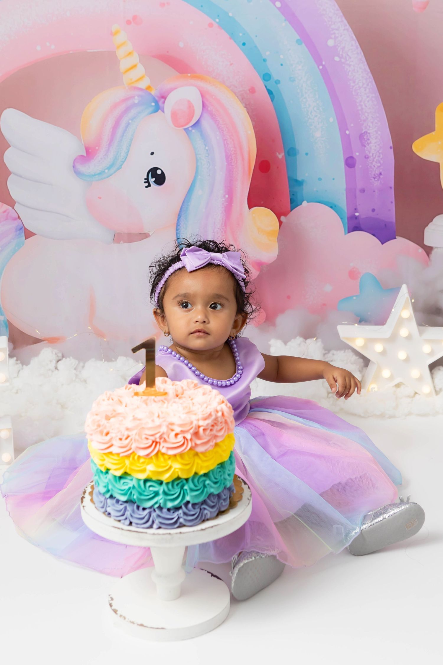 Unicorn themed first birthday with baby girl photographed with her cake